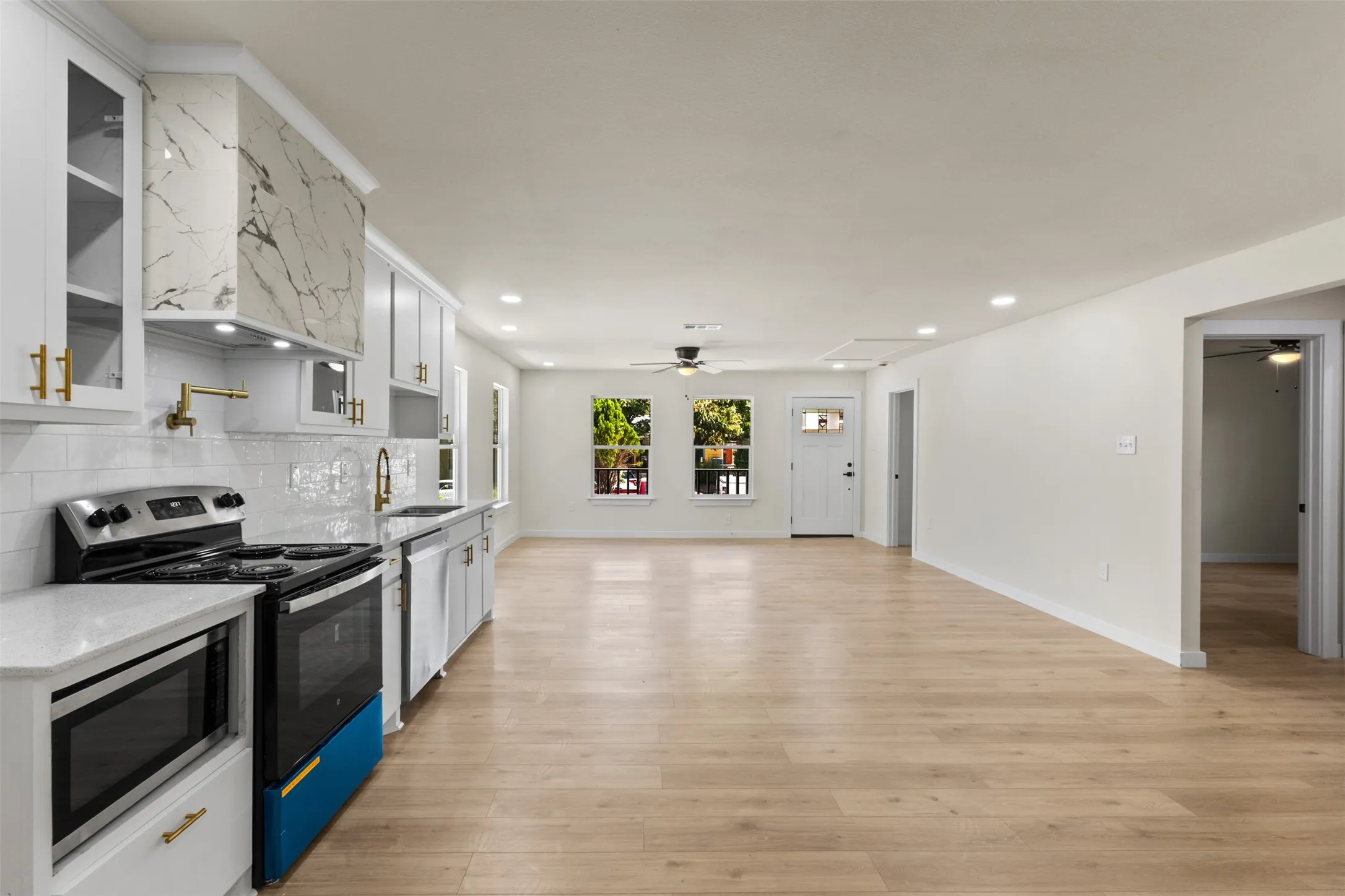 Open-concept kitchen and living area featuring white cabinetry with marble countertops, stainless steel appliances, subway tile backsplash, recessed lighting, and wide-plank wood-finish flooring throughout