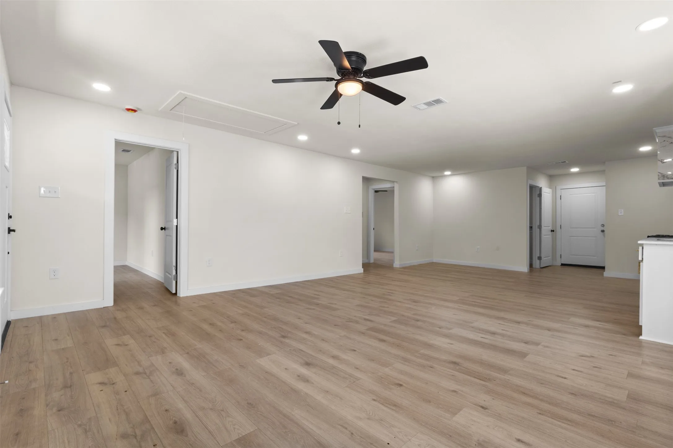 Spacious open-concept living area featuring engineered wood-finish flooring throughout, recessed ceiling lighting, and a ceiling fan with integrated light fixture