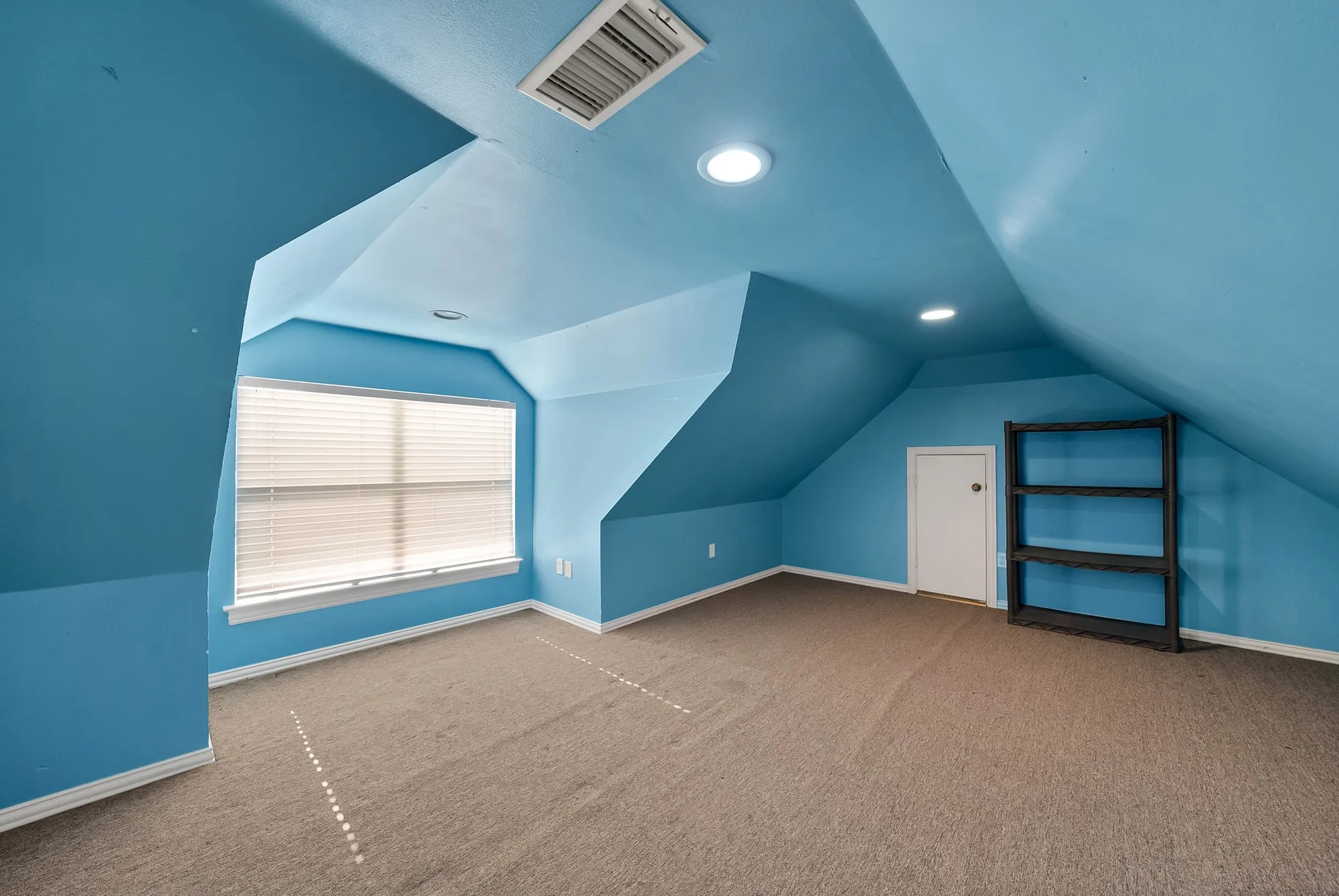 Carpeted room with sloped ceilings and a large window featuring blinds