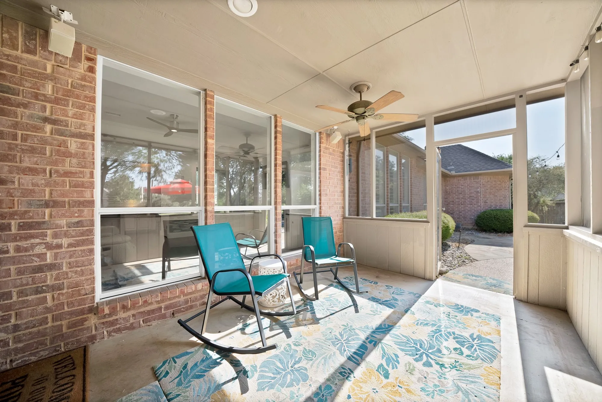 Screened sunroom featuring expansive windows with white frames, ceiling fan with brushed nickel finish, ceramic tile flooring, and patterned area rug