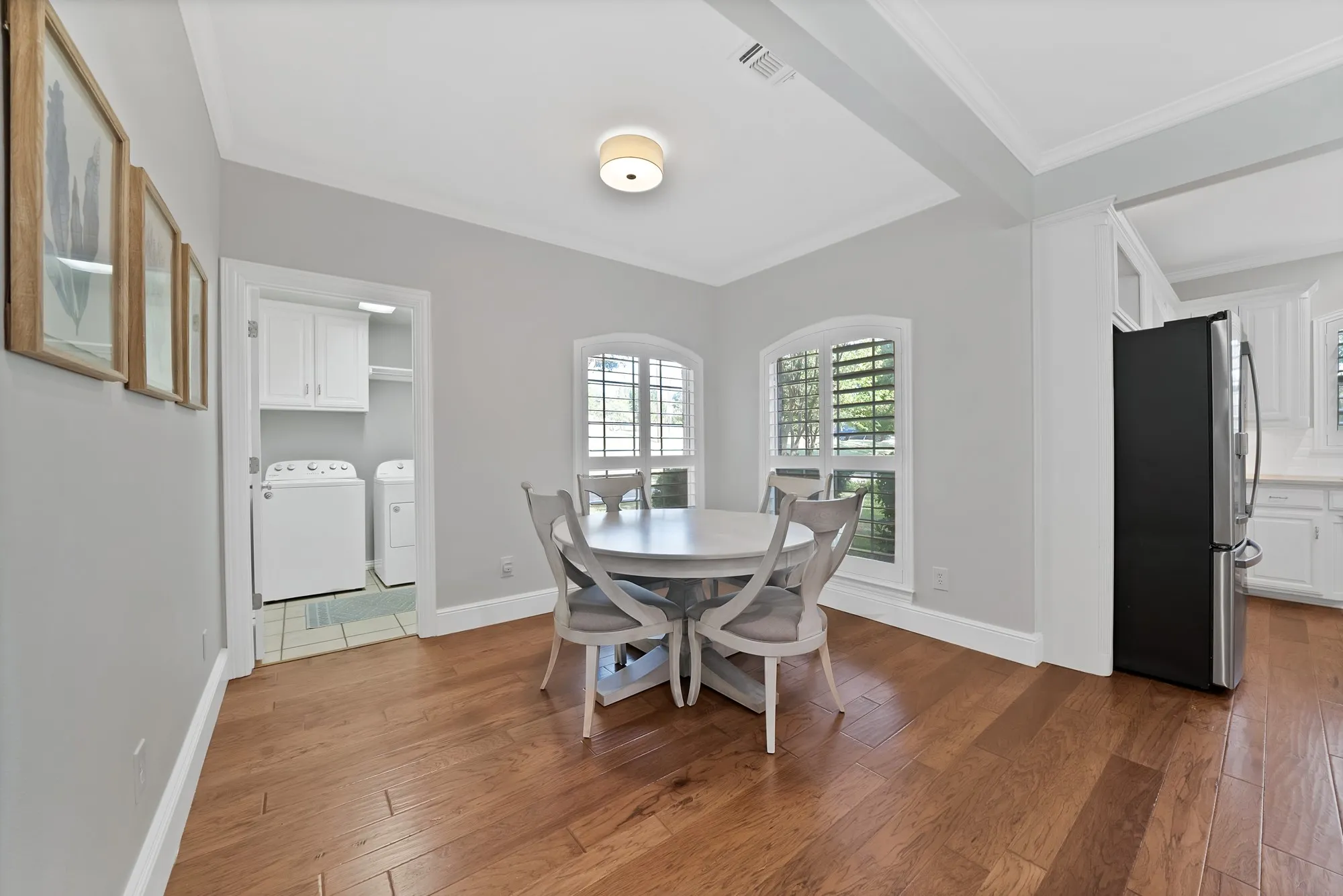 Dining area with wood-finish flooring, two arched windows with plantation shutters, crown molding, and a drum light fixture