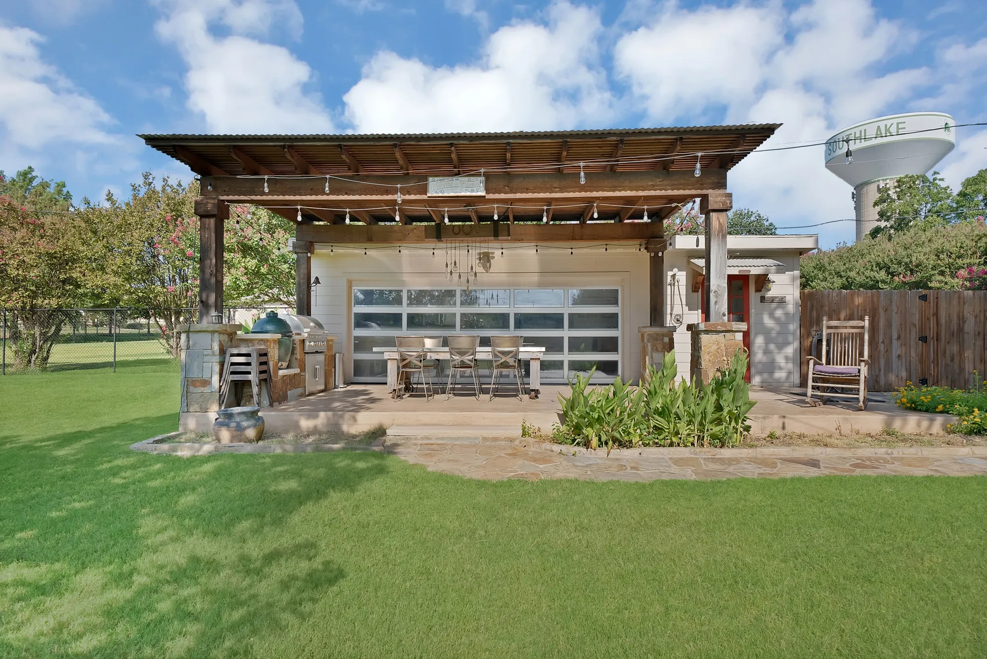 Outdoor entertaining area featuring a wood pergola with a corrugated metal roof, a built-in outdoor kitchen with stone accents, a concrete patio, and a modern glass-paneled garage door
