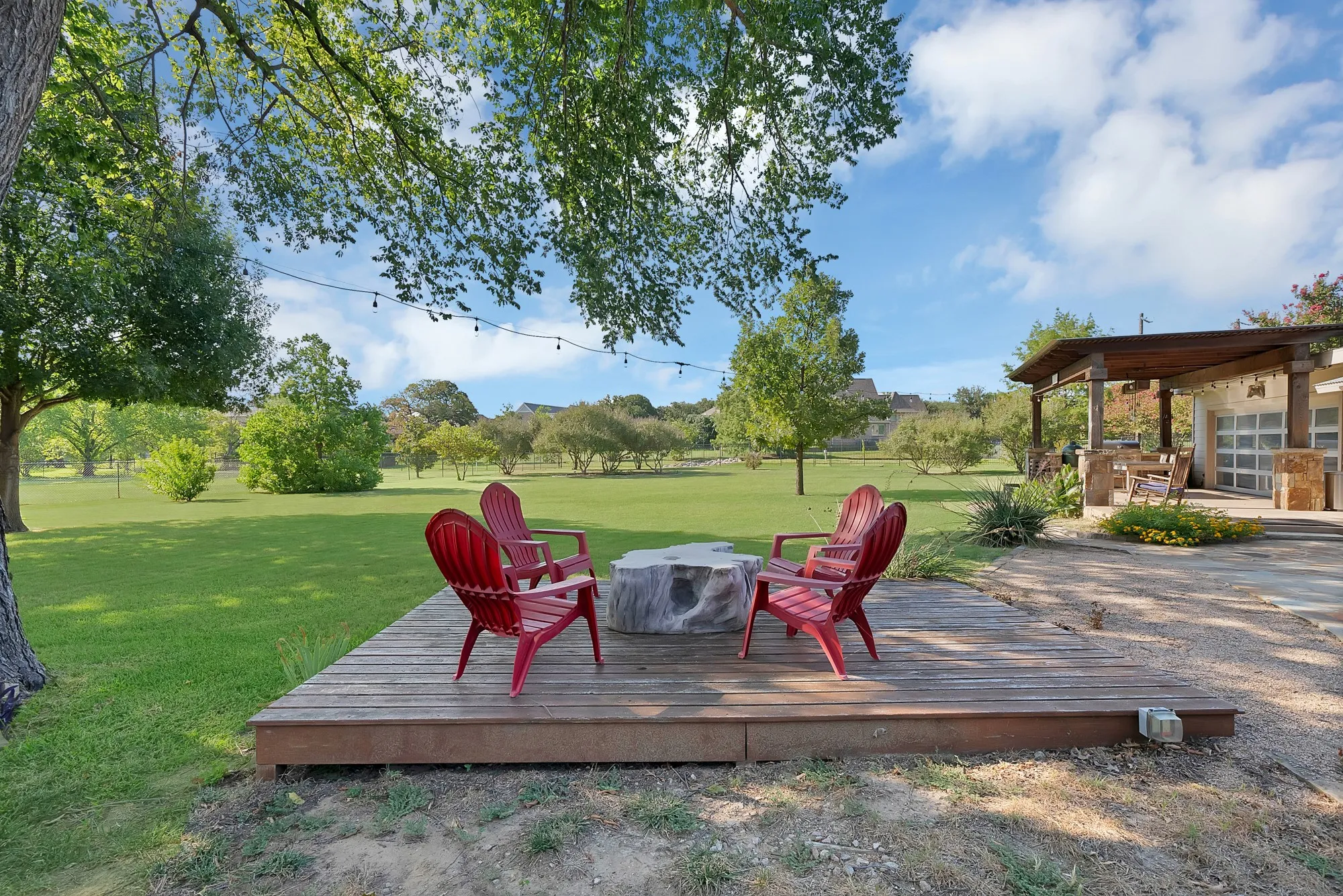 Expansive outdoor entertaining space featuring a composite deck with integrated fire pit, paired Adirondack seating, and mature landscaping