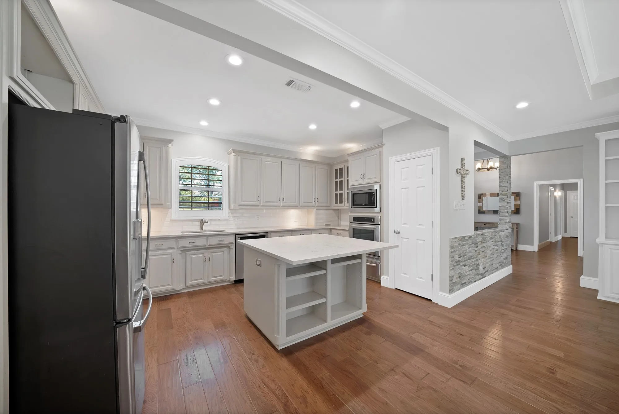 Spacious kitchen featuring white cabinetry, a large center island with storage and countertop seating, stainless steel appliances, quartz countertops, and wood-finish flooring throughout
