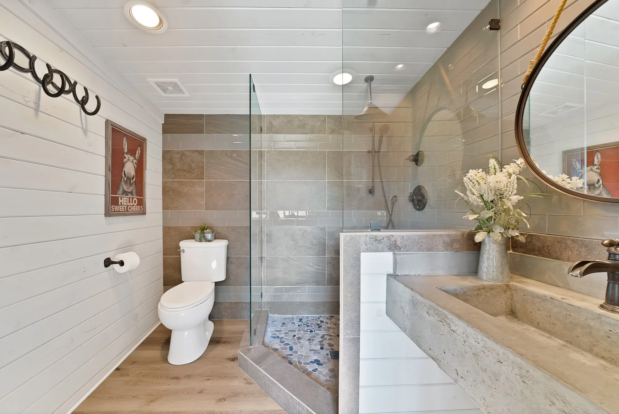 Bathroom featuring a glass-enclosed shower with pebble-tile flooring, a floating stone-finish vanity with an integrated basin, and wood-finish flooring