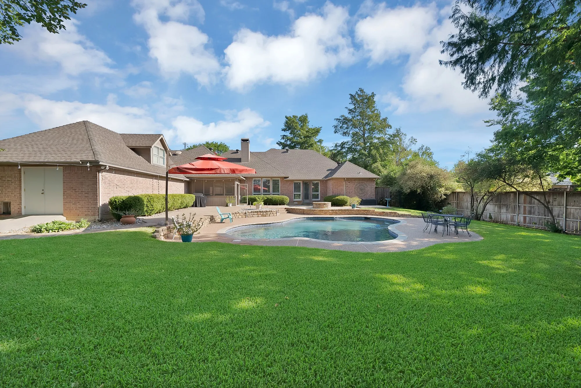 Expansive backyard oasis featuring a resort-style in-ground pool with sun deck, mature landscaping, and lush lawn