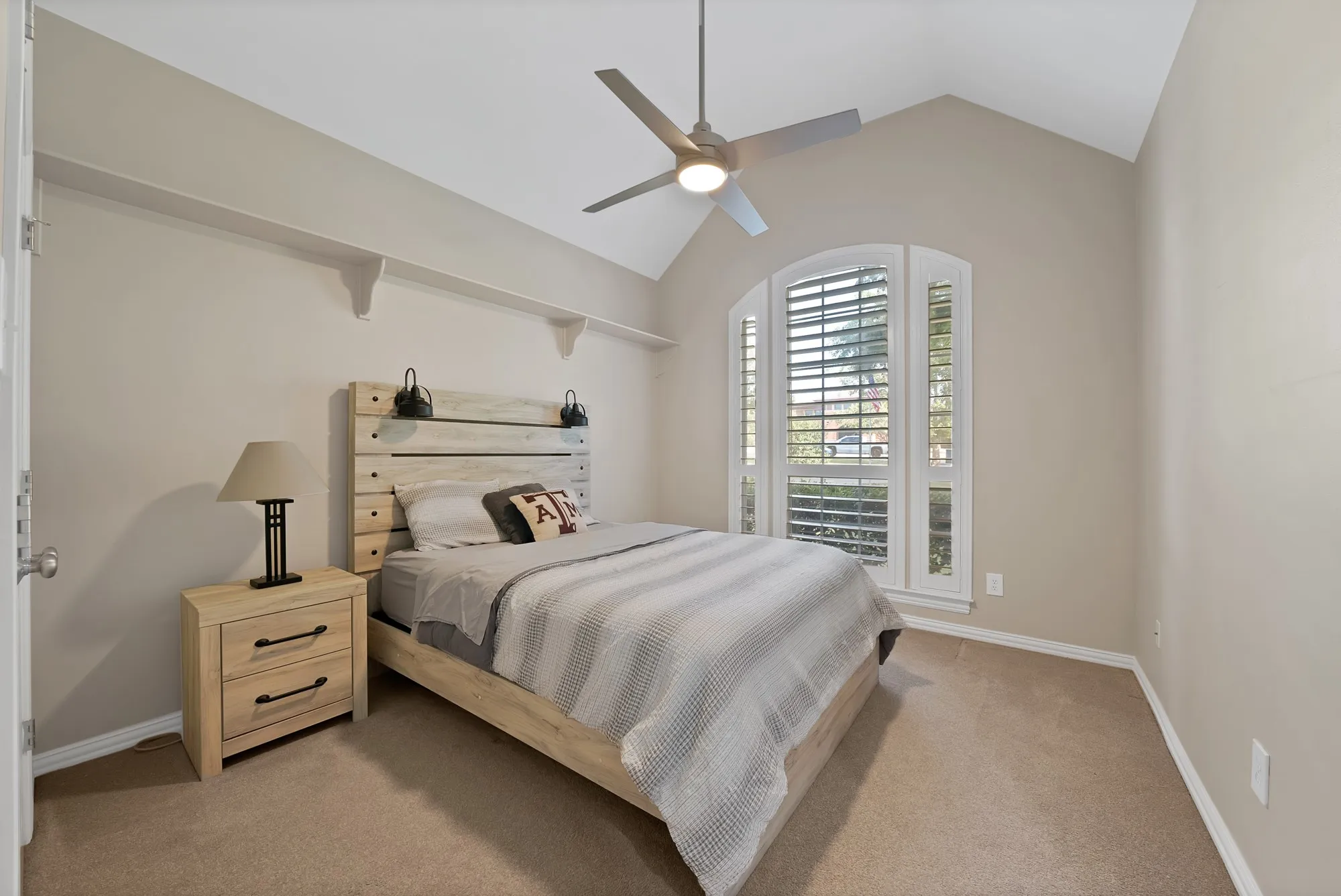 Vaulted ceiling bedroom featuring an arched window with plantation shutters, ceiling fan, and carpet flooring