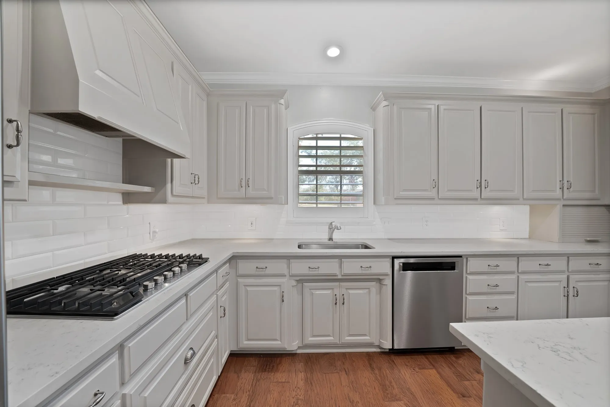Kitchen featuring white shaker-style cabinetry, a gas cooktop, stainless steel dishwasher, white subway tile backsplash, and light-colored countertops