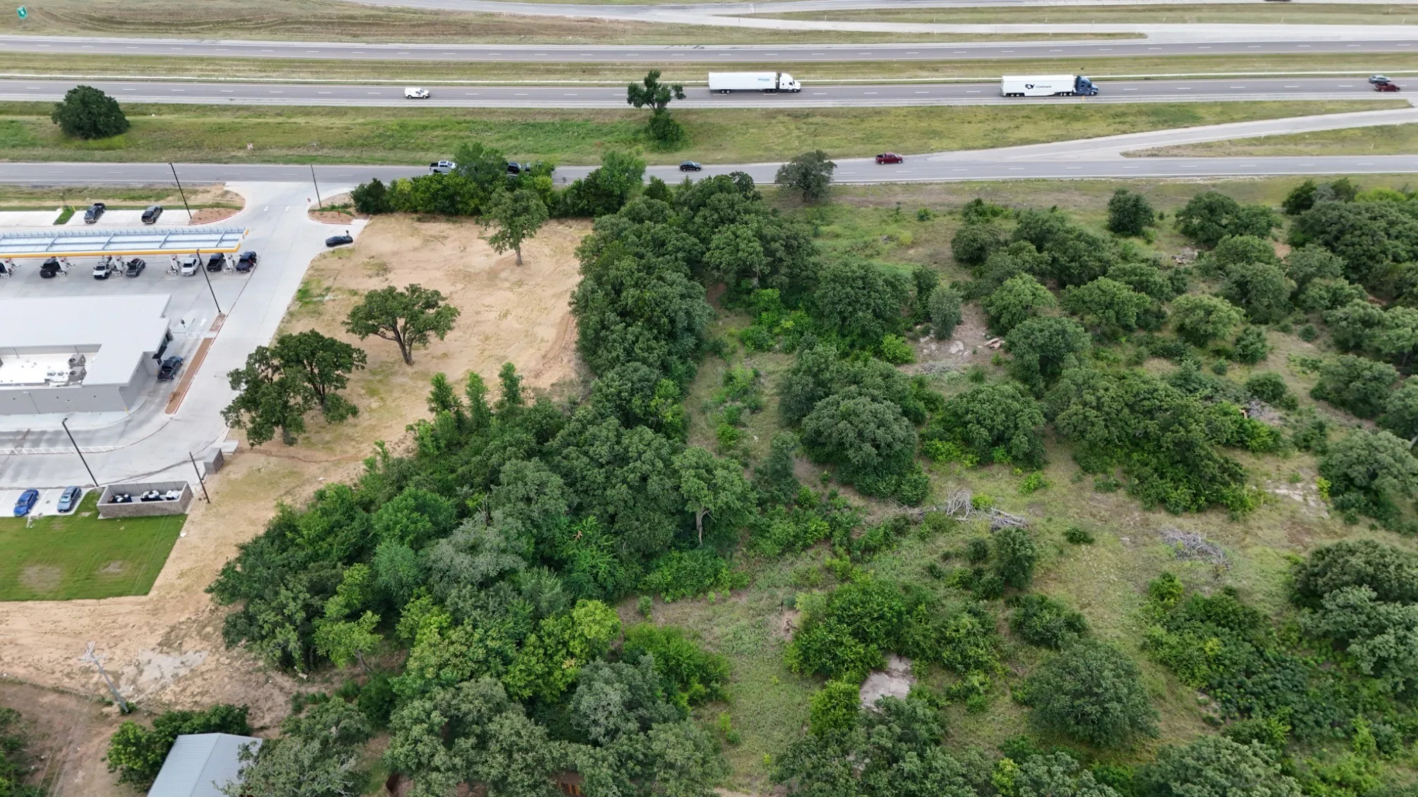 Expansive wooded property featuring mature trees and natural landscaping, with direct highway access and adjacent commercial parking areas
