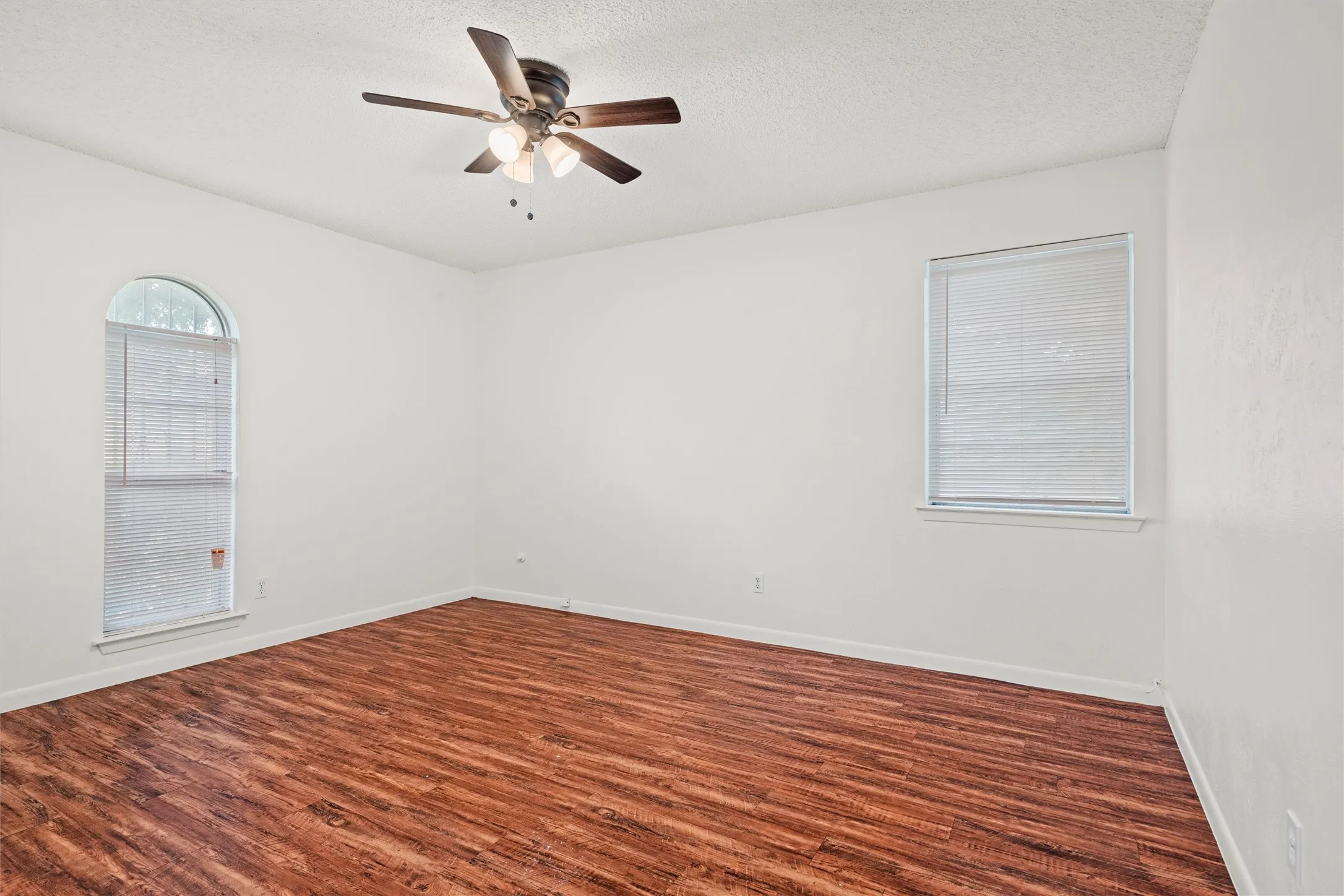 Natural light, warm wood-look flooring, neutral walls, and a charming arched window create a comfortable bedroom that’s ready for your personal touch.