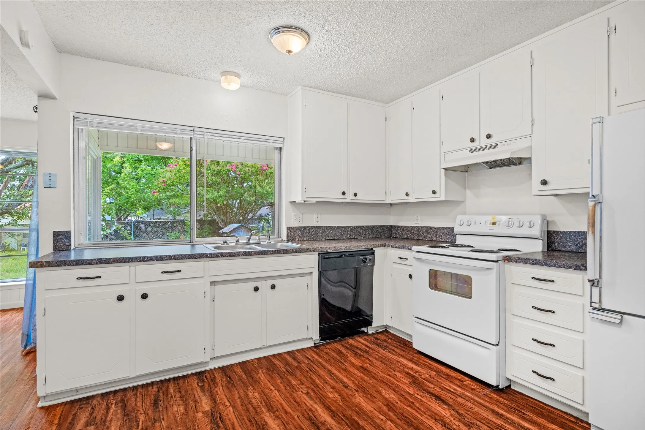 Natural light pours through the oversized window above the sink, offering a peaceful view of the backyard. Generous cabinetry and wraparound counter space make everyday cooking and entertaining feel effortless.