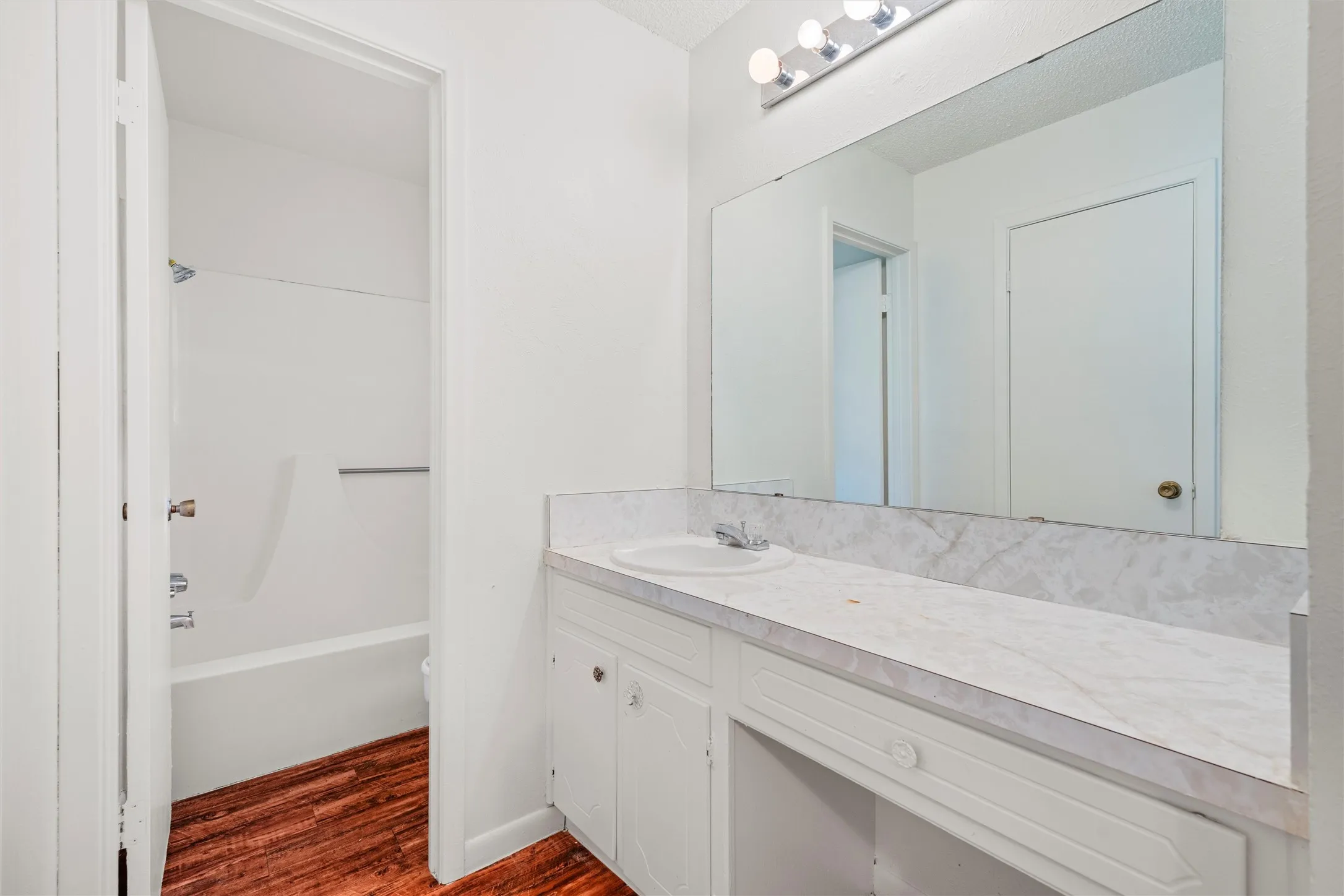 Bright and functional, this full bathroom offers an extended vanity, oversized mirror, generous counter space, and a tub-and-shower combination designed for everyday convenience.