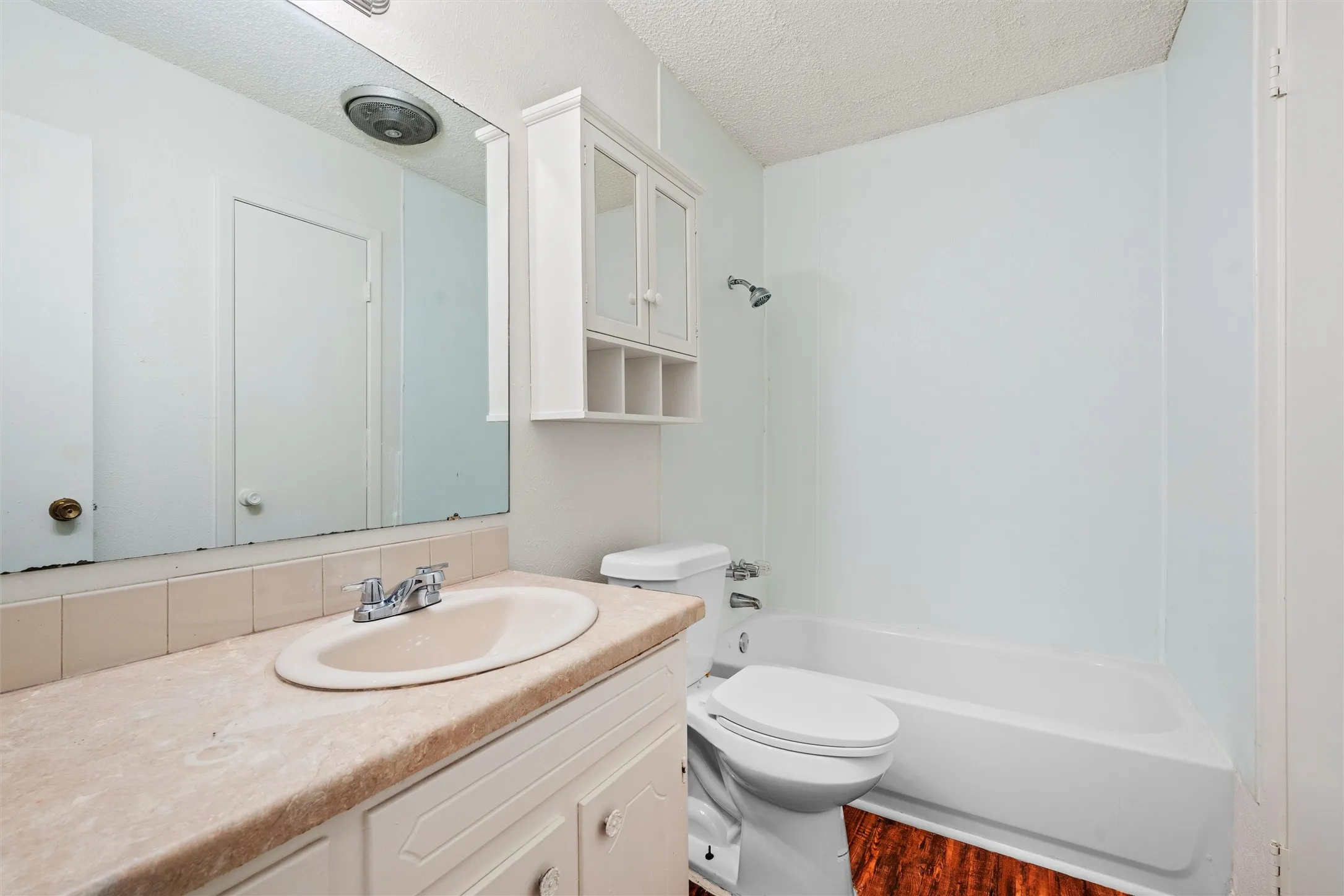 This full bathroom brings together a tub-and-shower combination, extended mirror, vanity storage, and additional wall cabinetry for convenient everyday organization.
