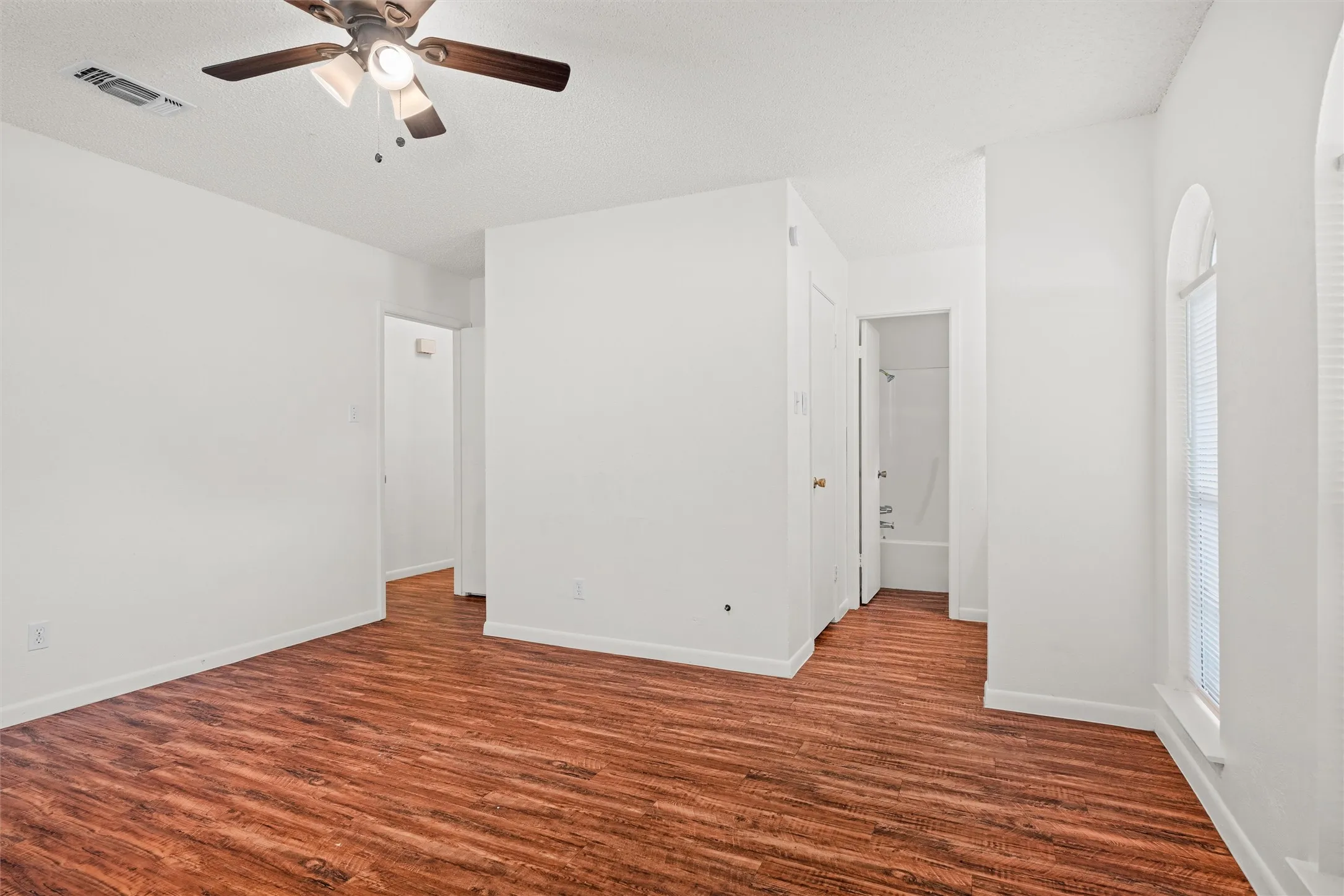 This spacious bedroom combines beautiful flooring, abundant natural light, a ceiling fan, generous wall space, and convenient access to the adjoining bathroom—perfect for relaxing and recharging.
