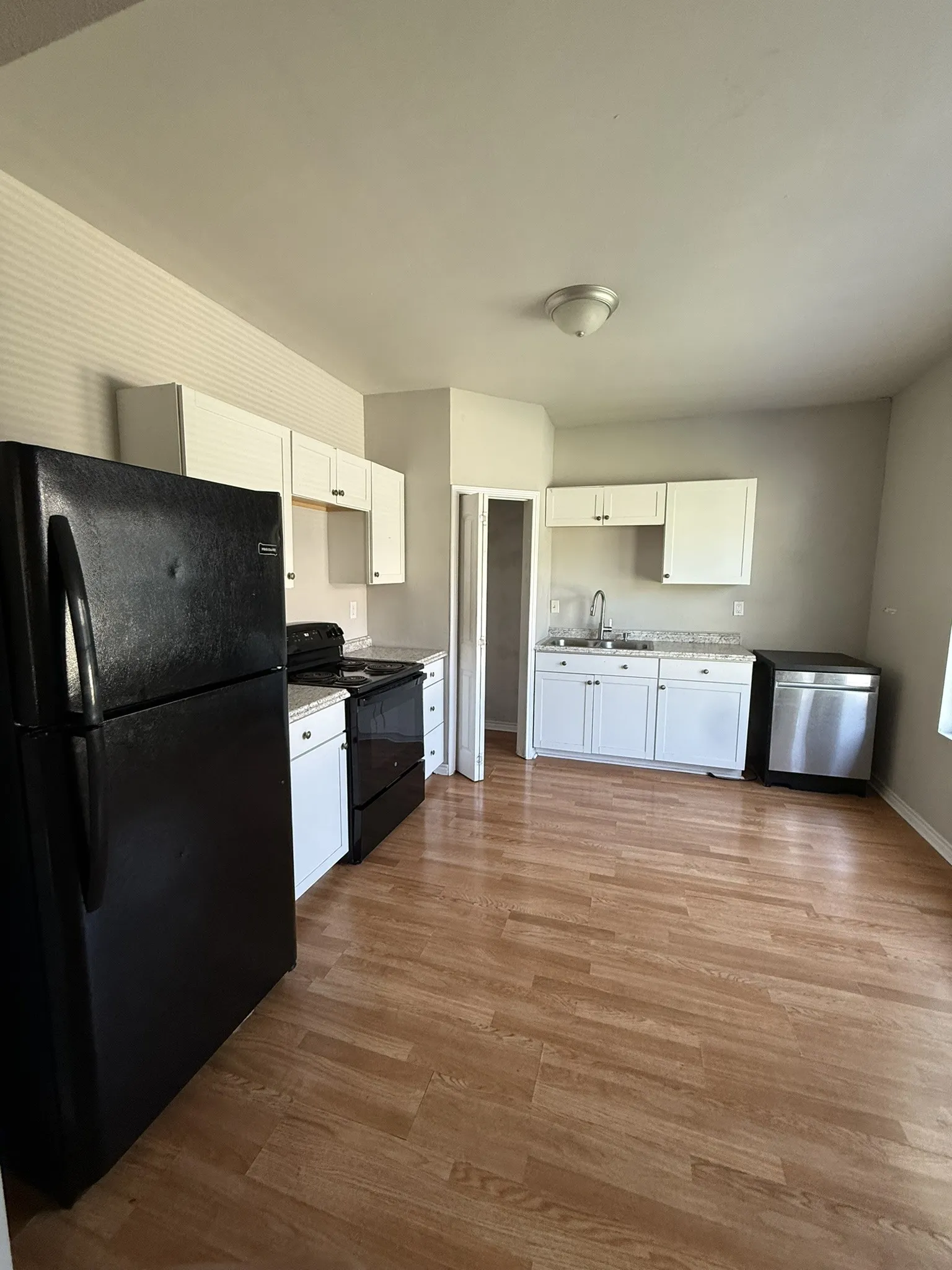 Kitchen featuring wood-finish flooring, white cabinetry, black appliances, stainless steel dishwasher, and a ceiling-mounted light fixture