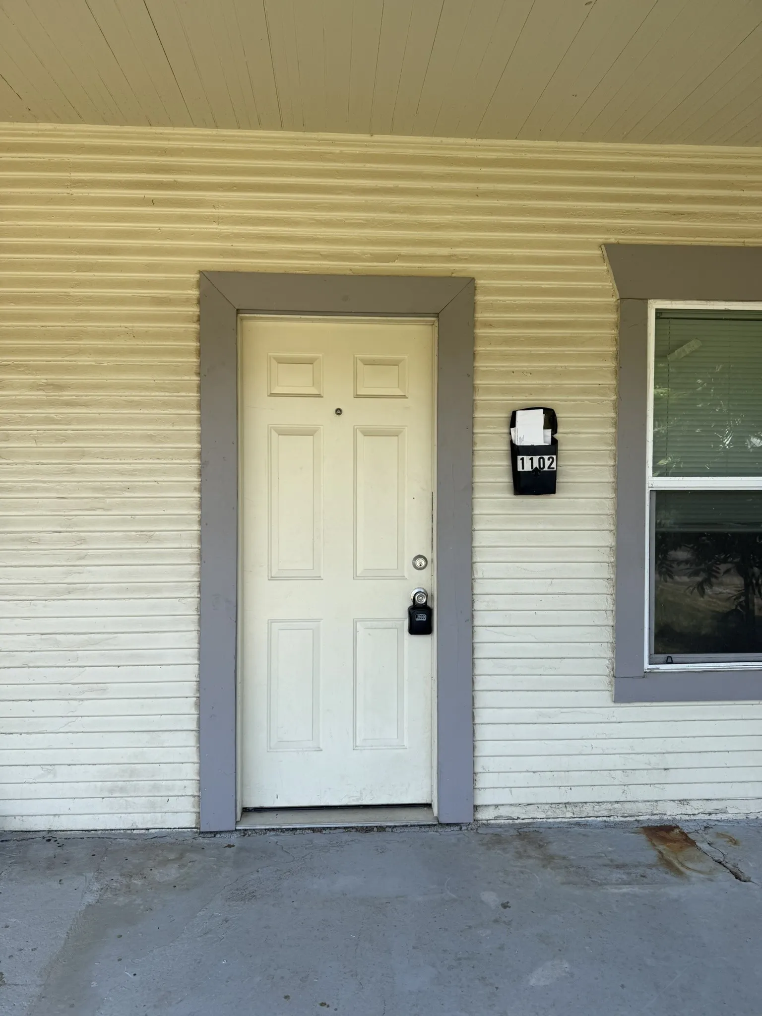 White paneled entry door with gray trim, featuring a wall-mounted mailbox and horizontal siding