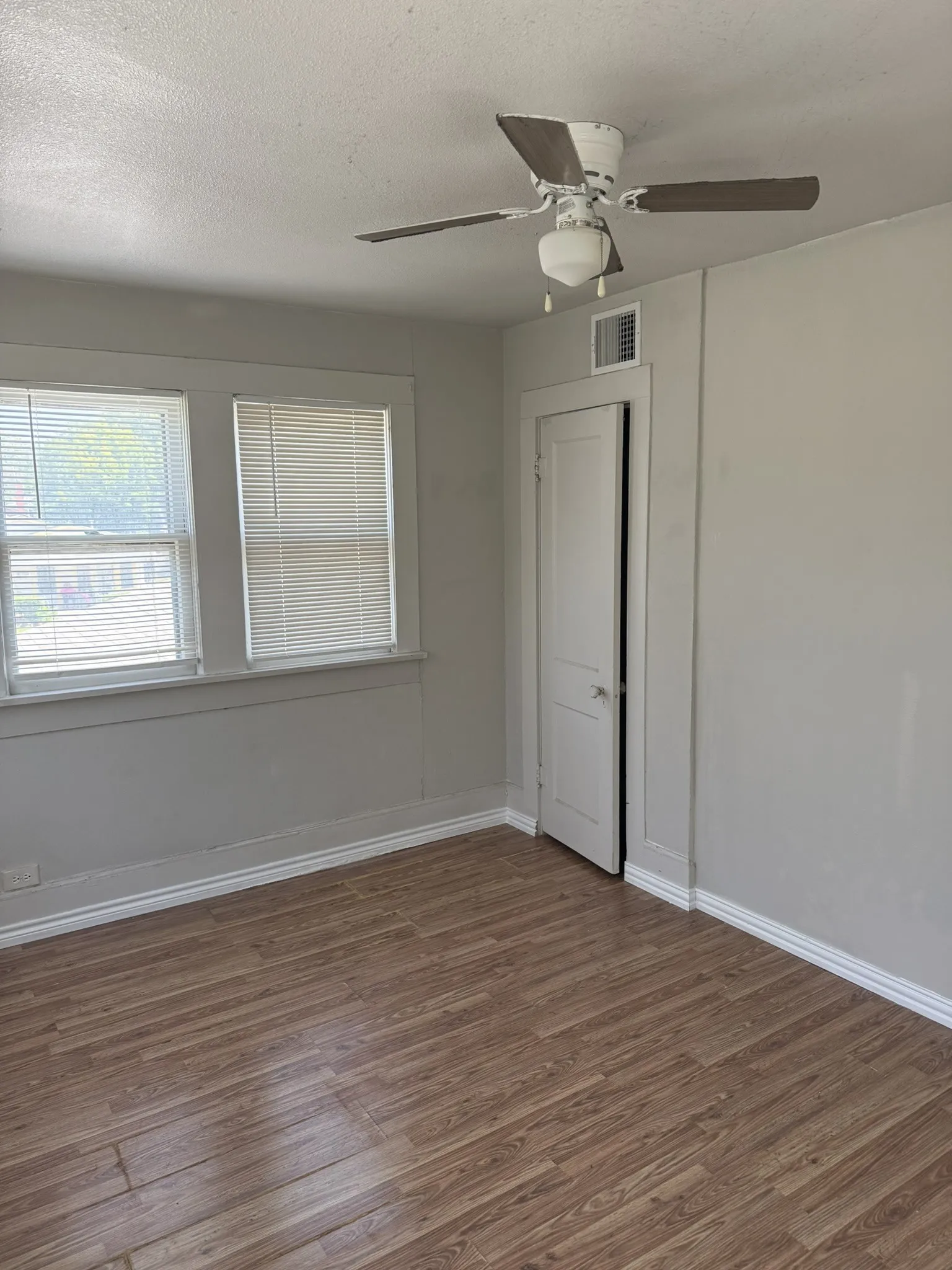 Upstairs bedroom #2 Bright, spacious bedroom featuring wood-finish flooring, large double-hung windows with blinds providing natural light, ceiling fan with integrated lighting fixture, and a clean, neutral color palette throughout