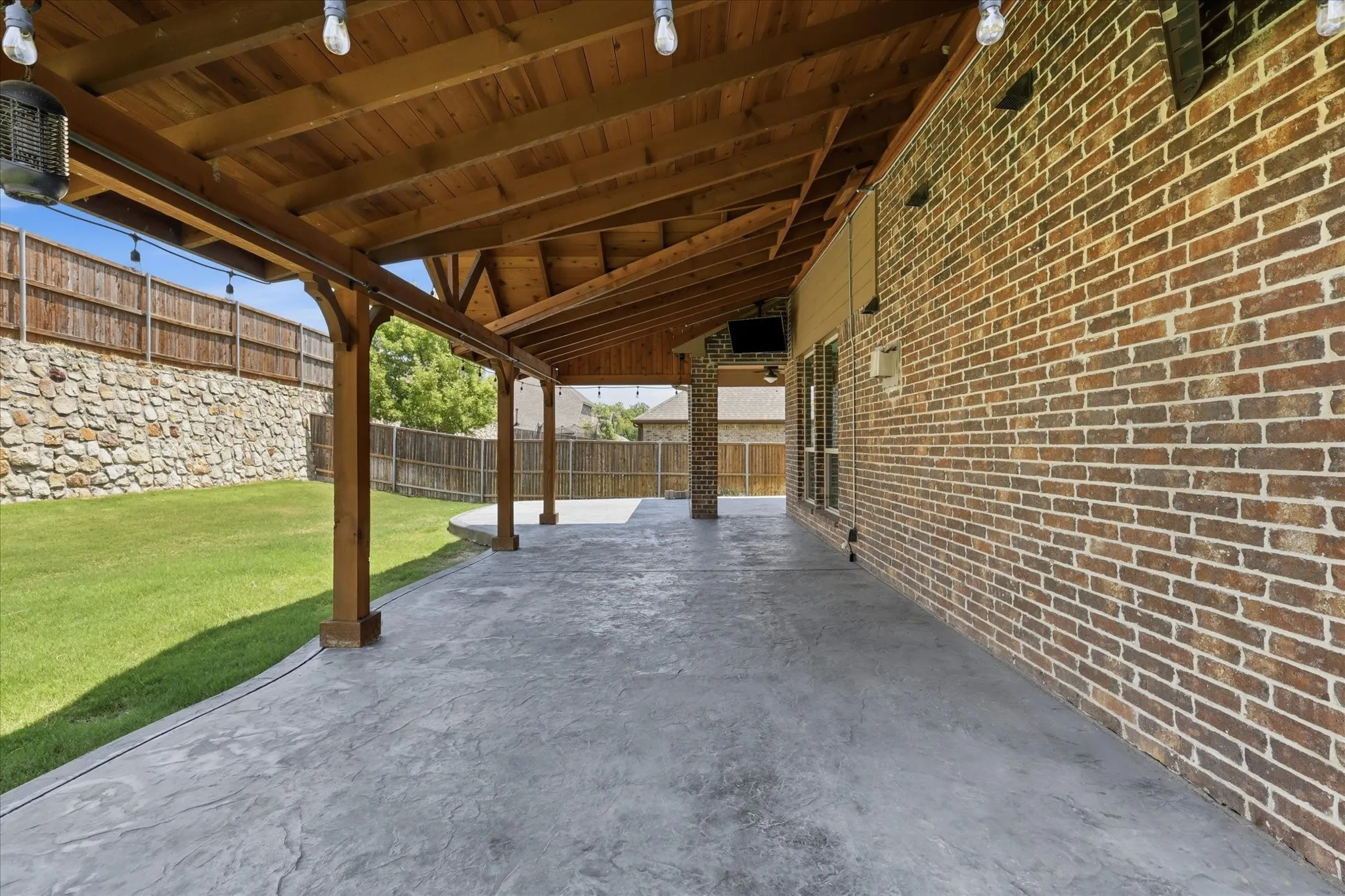 Stamped concrete batio extends the entire length of the home and upgraded vaulted roof has bistro lights and two mounted TVs