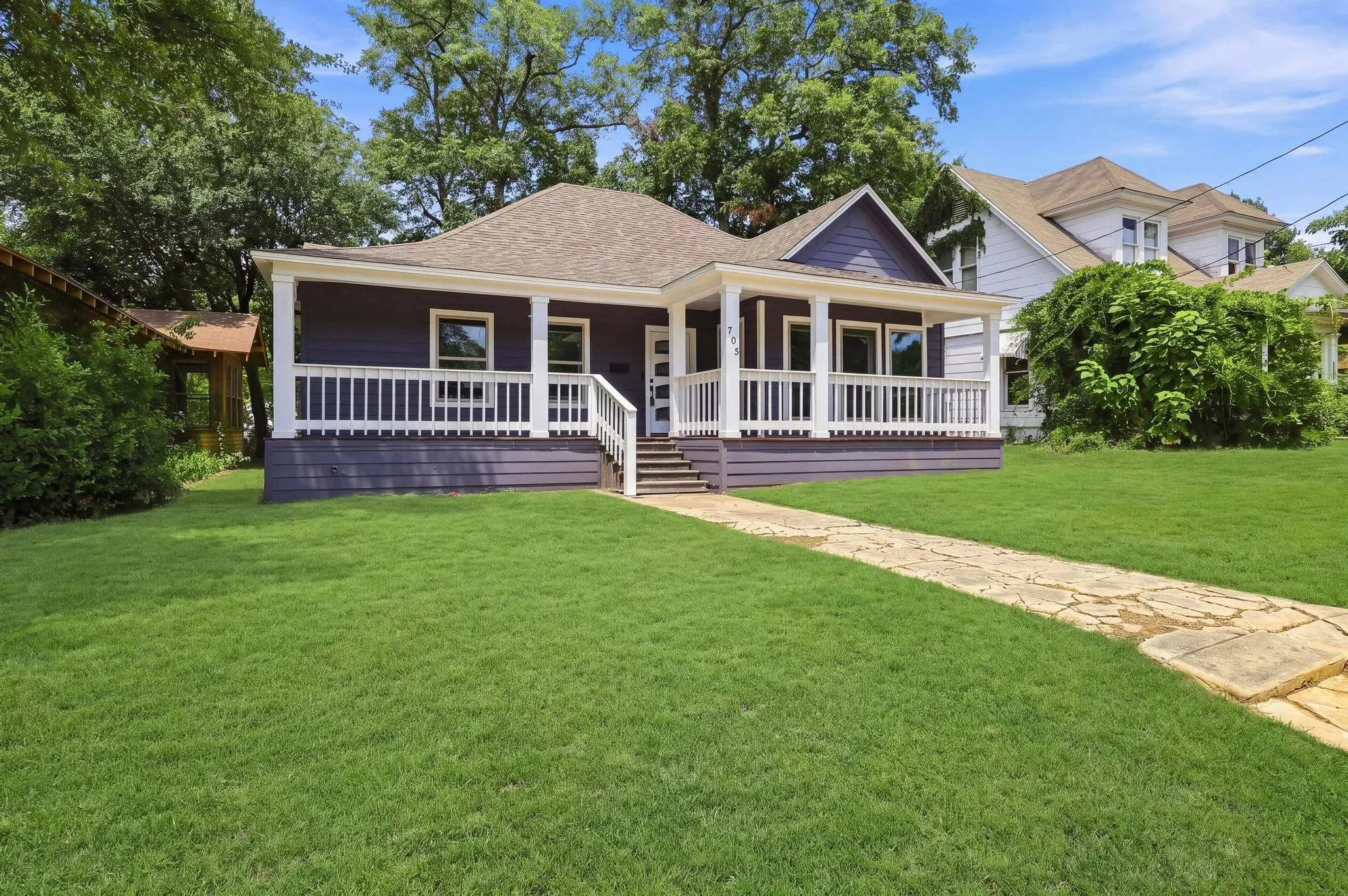 Single-story residence featuring a covered front porch with white railing, a stone-paved walkway, and a landscaped front lawn