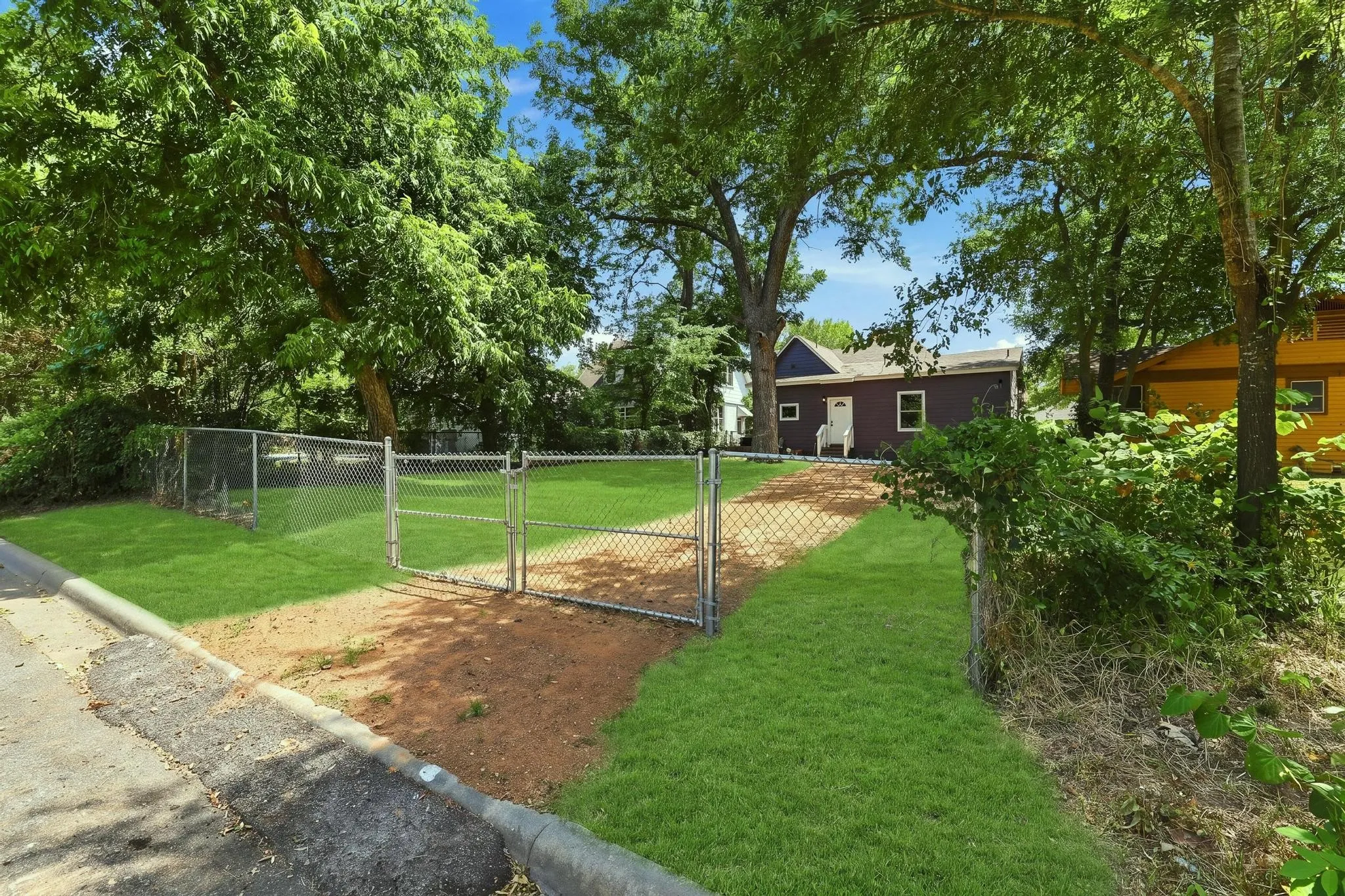 Manicured lawn, mature trees, chain-link fencing, and a gravel pathway