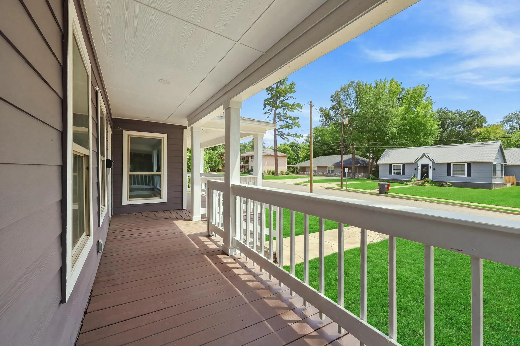 Covered front porch with wood-finish flooring, white railing, and exterior siding