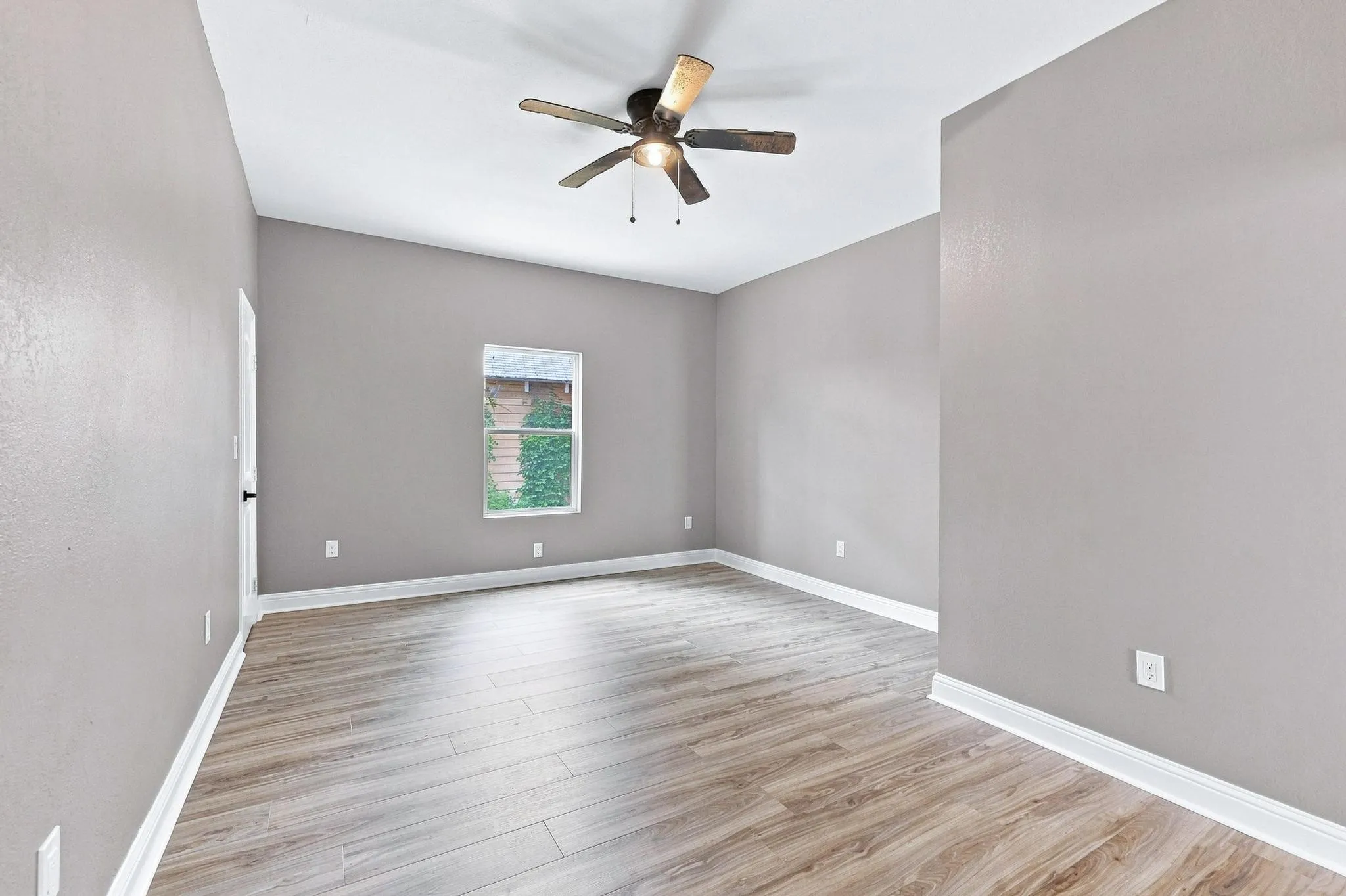 Vaulted ceiling with a ceiling fan, wood-finish flooring, a single window, and neutral wall tones