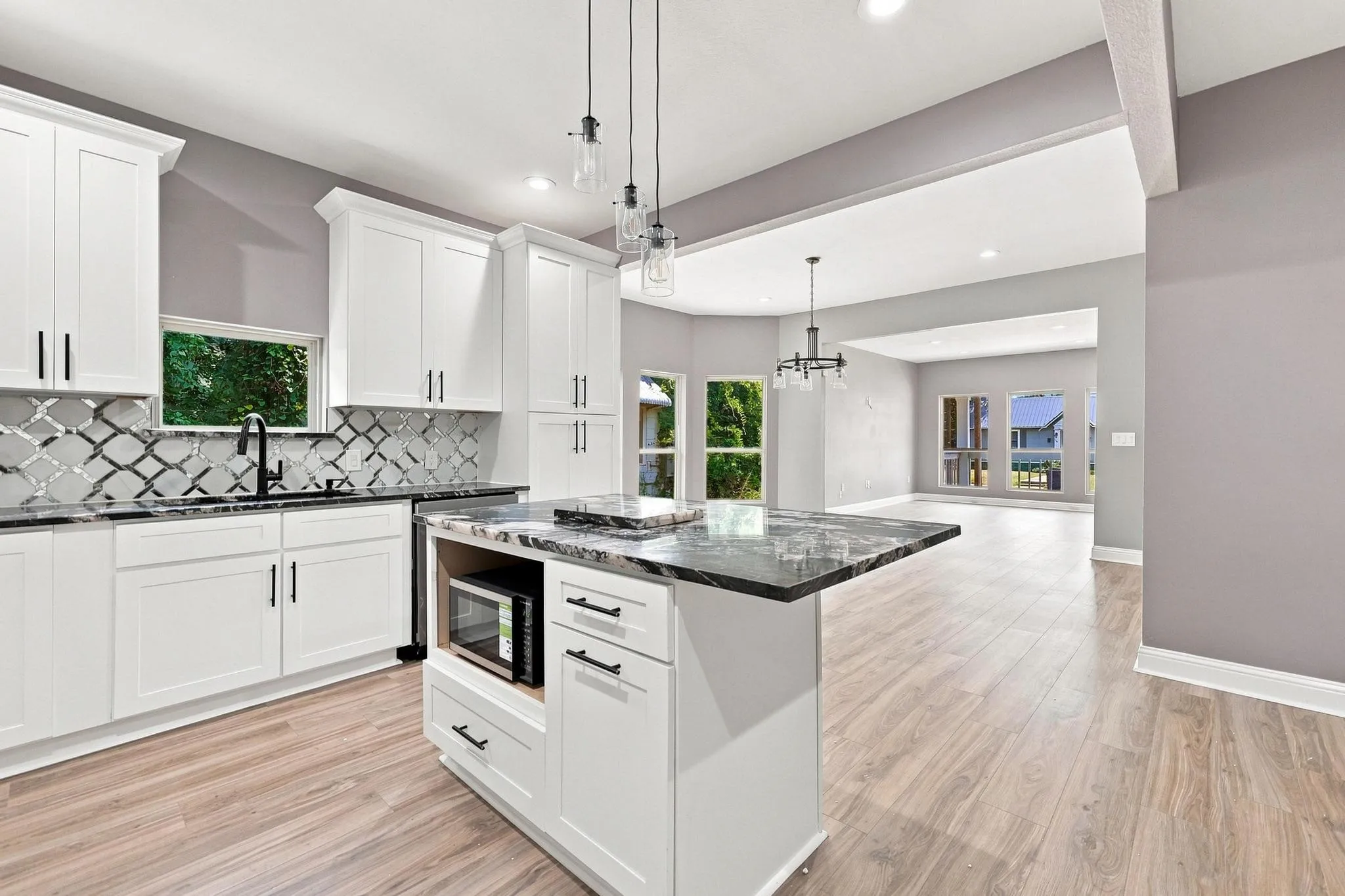 Kitchen featuring white cabinetry with black hardware, dark countertops, a decorative tile backsplash, and wood-finish flooring