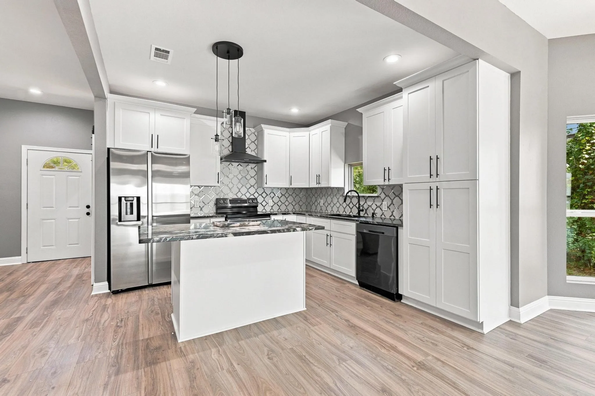 Kitchen featuring wood-finish flooring, white cabinetry with dark hardware, stainless steel refrigerator, patterned tile backsplash, and a central island with a stone countertop