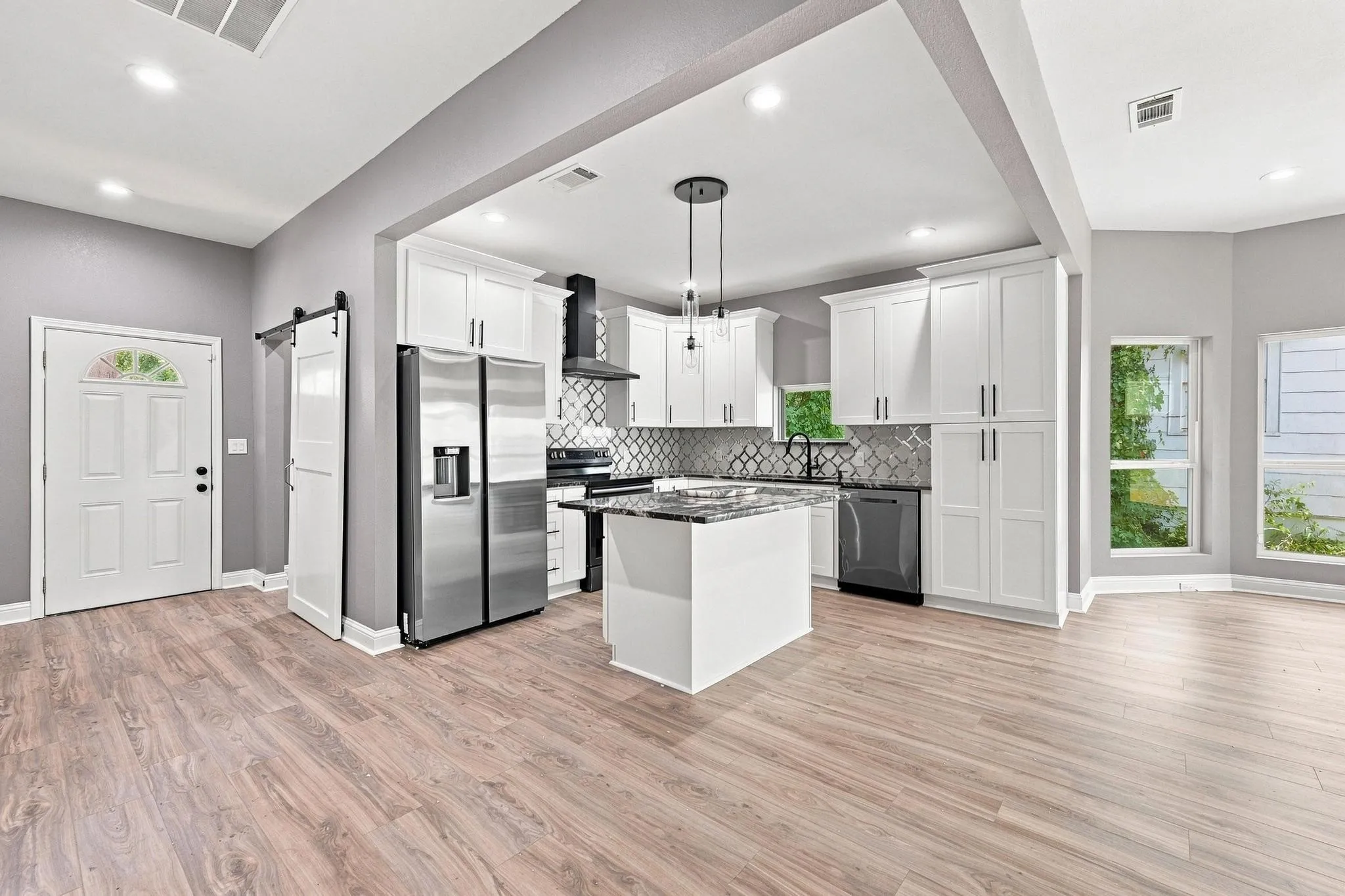 Wood-finish flooring throughout, white shaker-style cabinetry, stainless steel appliances, kitchen island with counter seating, and recessed lighting