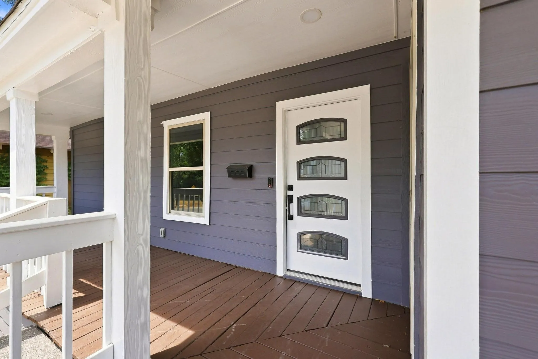 Covered front porch with wood-finish flooring, white railing, and white columns