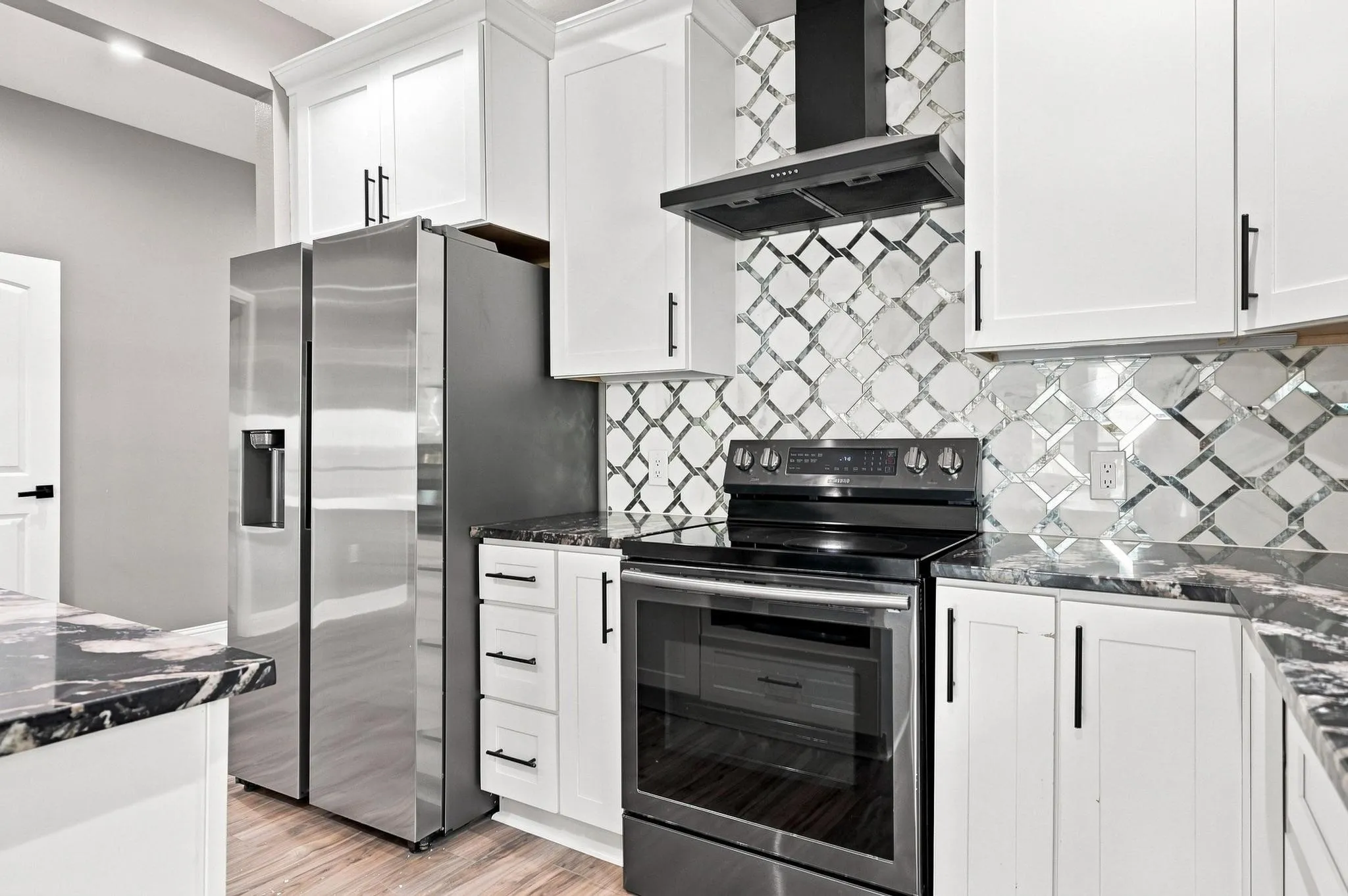 Modern kitchen featuring white shaker cabinetry, stainless steel appliances including a gas range with black hood, quartz countertops, and a geometric tile backsplash