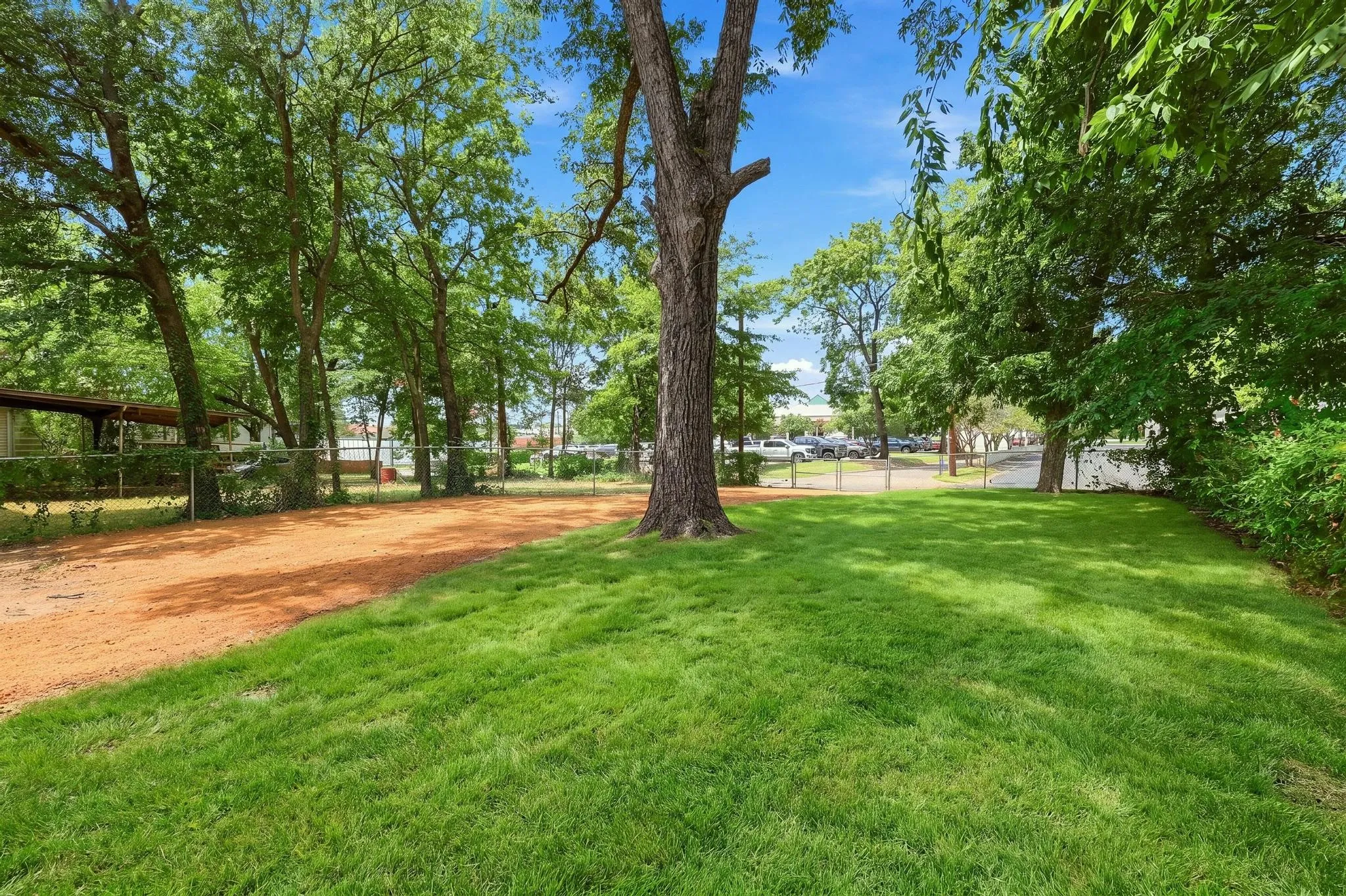 Expansive outdoor area featuring a manicured lawn, established mature trees, and a natural ground cover section