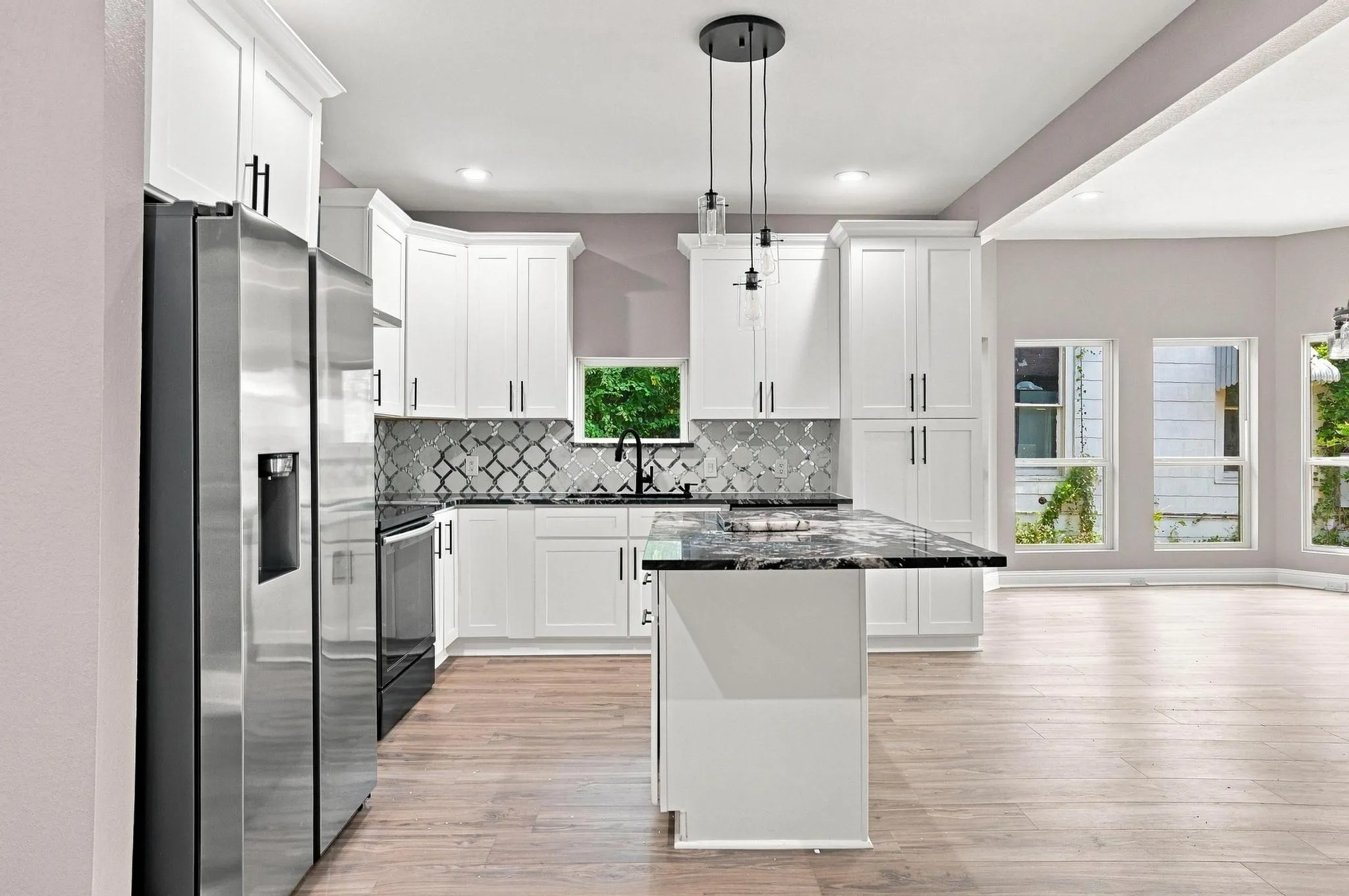 White shaker cabinetry, patterned tile backsplash, stainless steel appliances, black countertops, and light wood-finish flooring