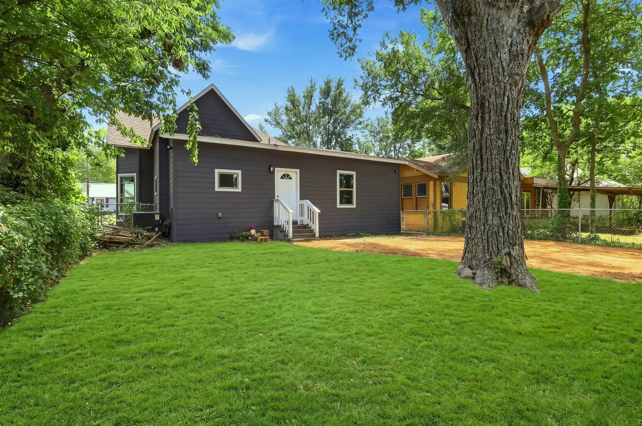 Expansive green lawn with mature trees and a dark gray siding exterior