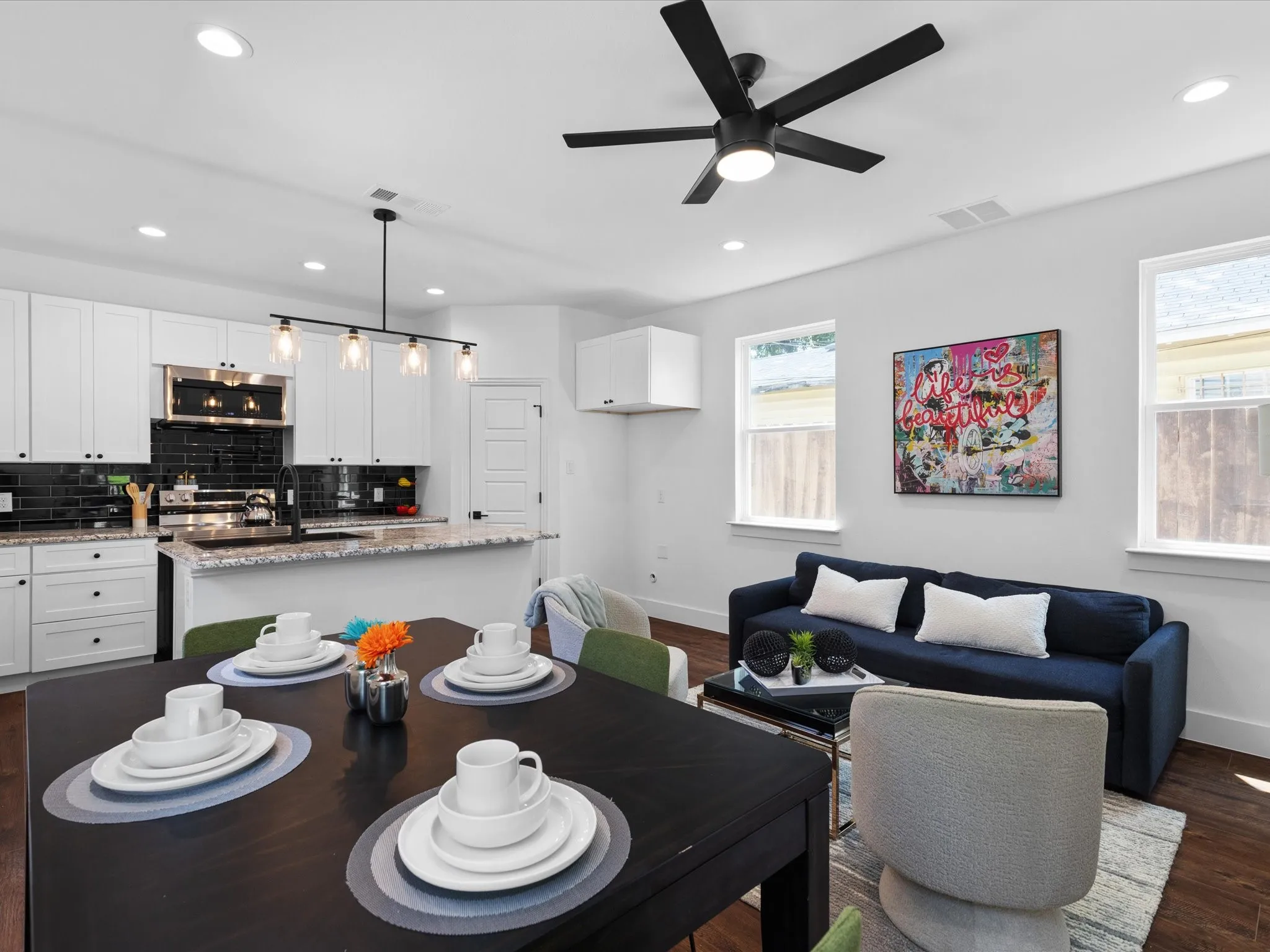Open-concept living space featuring a modern kitchen with white cabinetry, stainless steel appliances, and a black subway tile backsplash