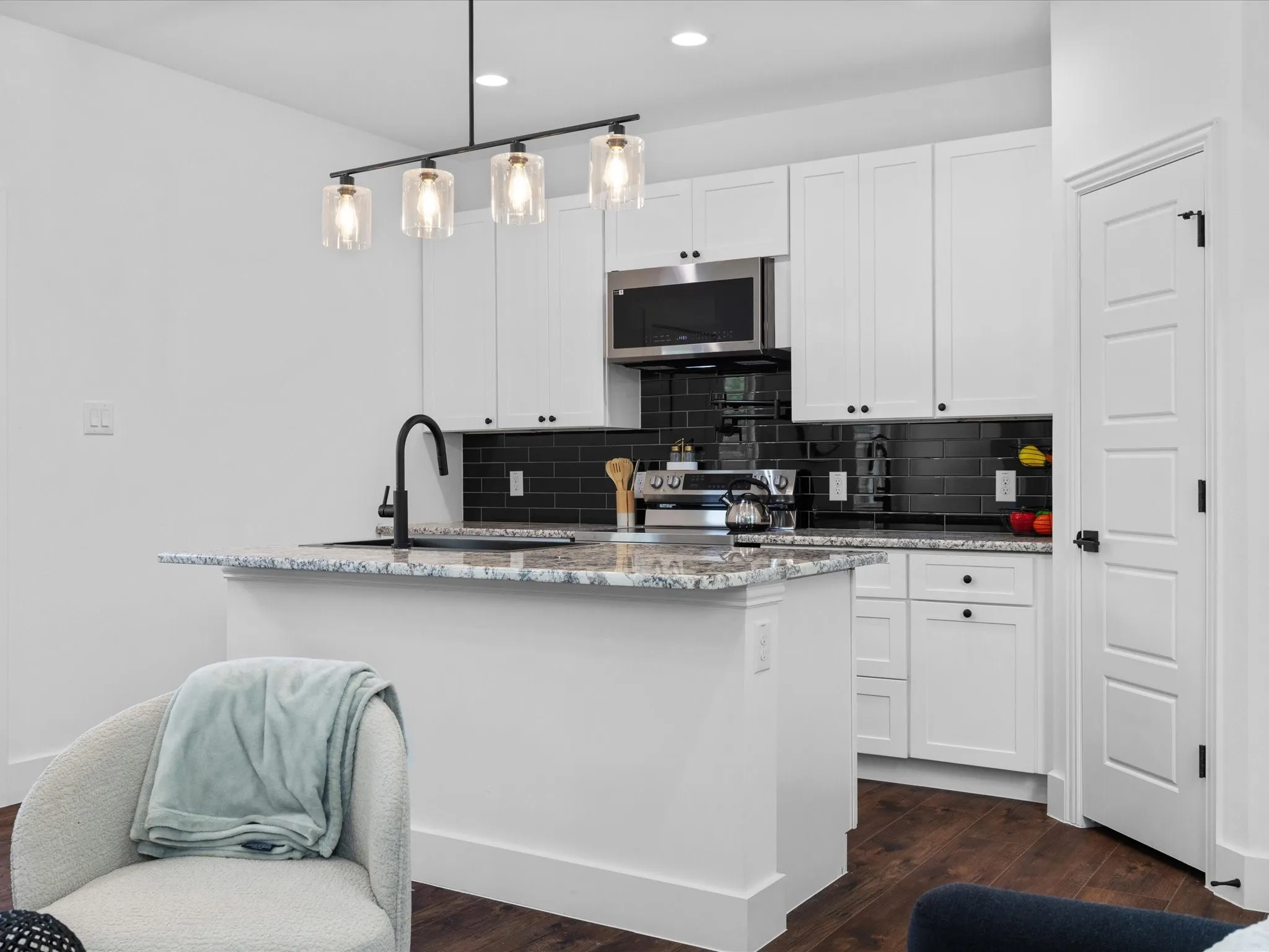 Modern kitchen featuring crisp white cabinetry, black subway tile backsplash, and a multi-level island with speckled quartz countertops