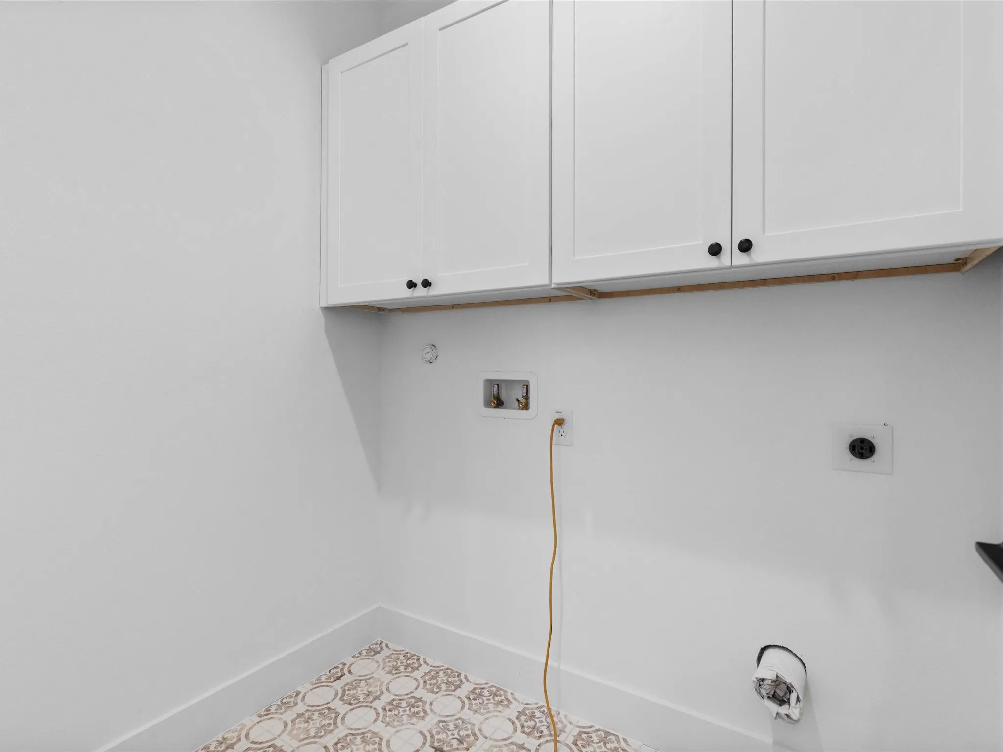 Dedicated utility space featuring patterned floor tile and white shaker cabinetry with dark hardware