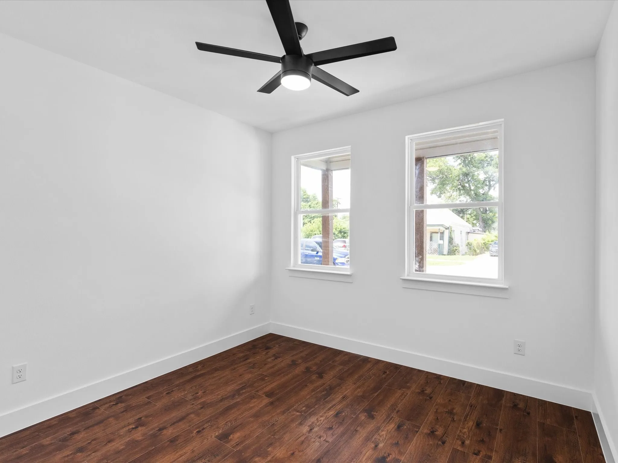 Bright interior featuring two windows, wood-finish flooring, a modern ceiling fan with integrated lighting, and white baseboards