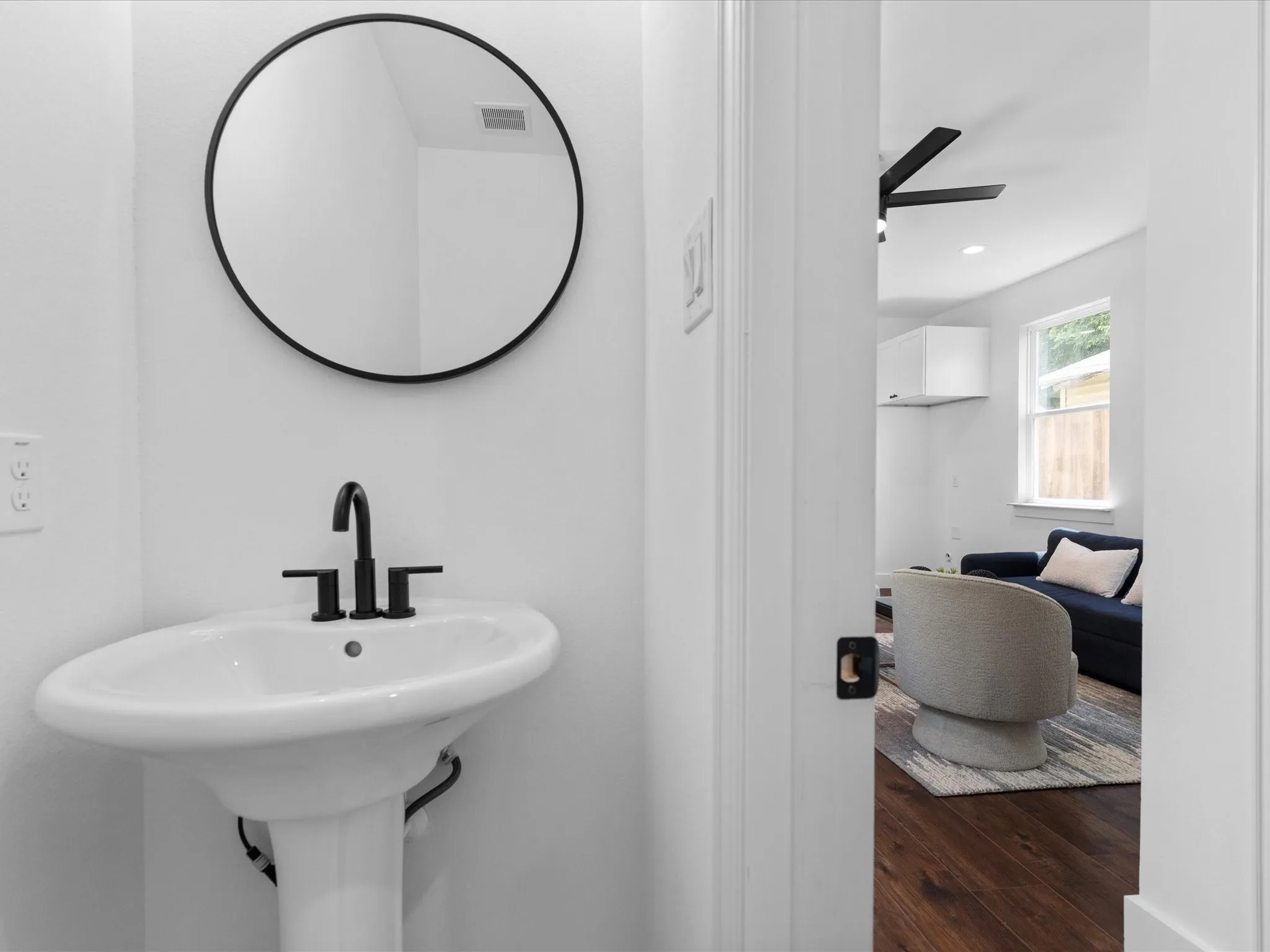 White pedestal sink with matte black faucet and a coordinating round mirror