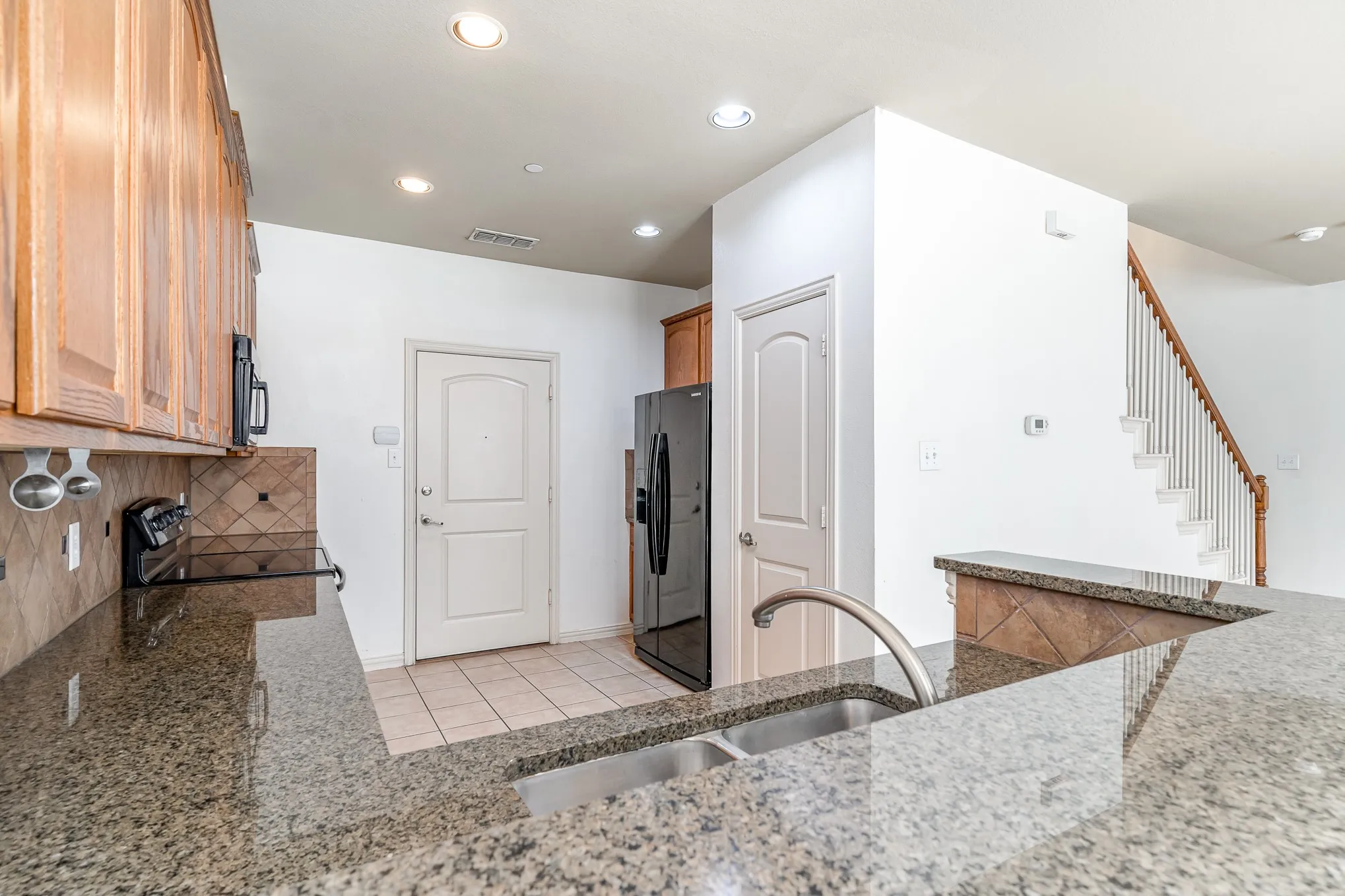 Kitchen with light stone countertops, black appliances, backsplash, sink, and light tile flooring