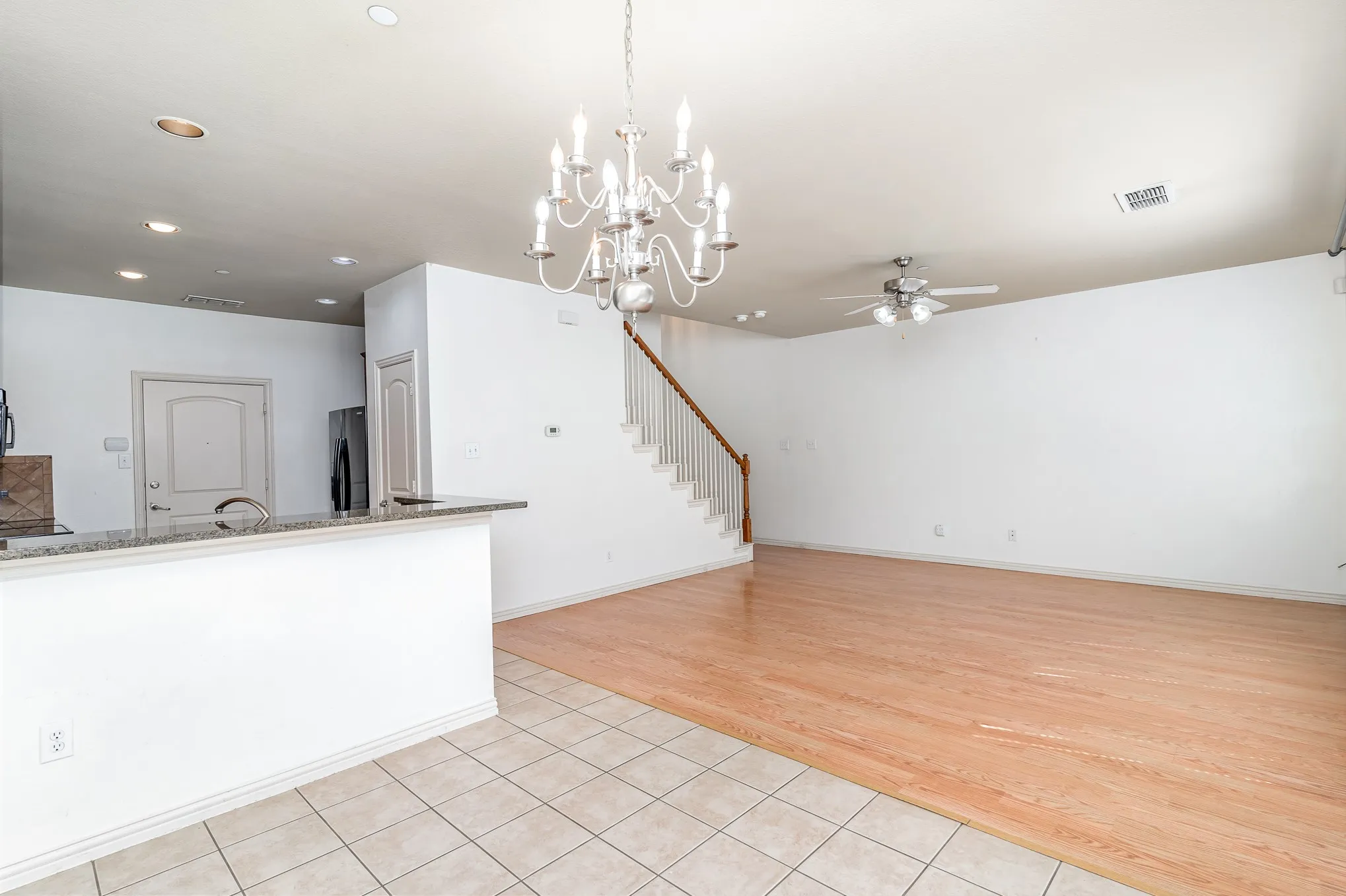 Unfurnished living room featuring sink, light tile flooring, and ceiling fan with notable chandelier