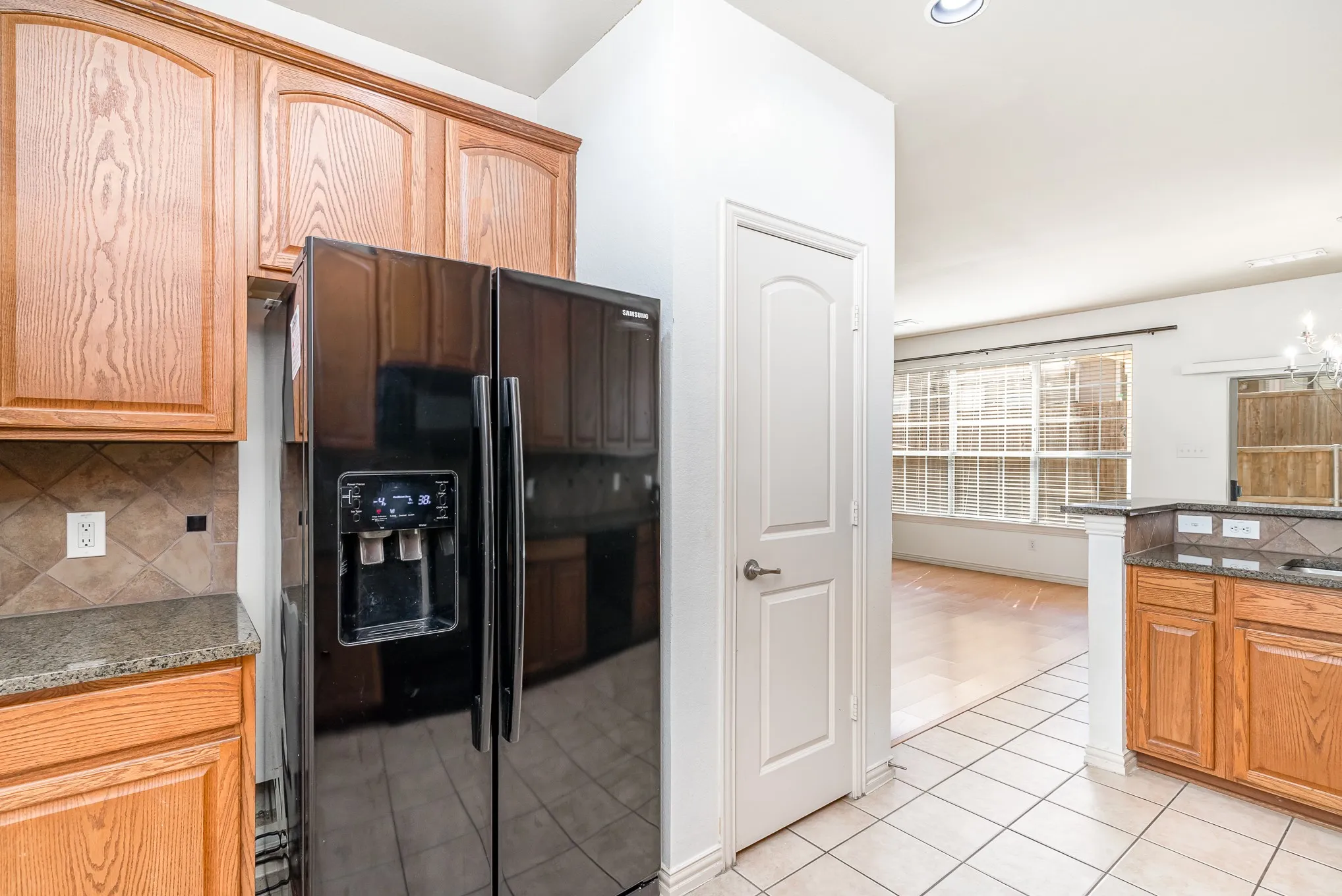 Kitchen with dark stone counters, black refrigerator with ice dispenser, light tile flooring, and tasteful backsplash