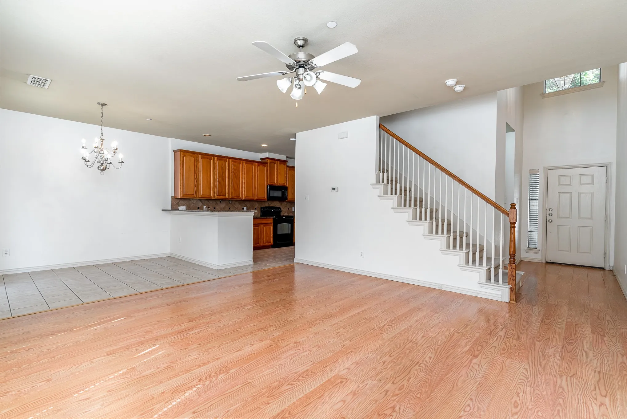 Unfurnished living room featuring a towering ceiling, light wood-type flooring, and ceiling fan with notable chandelier