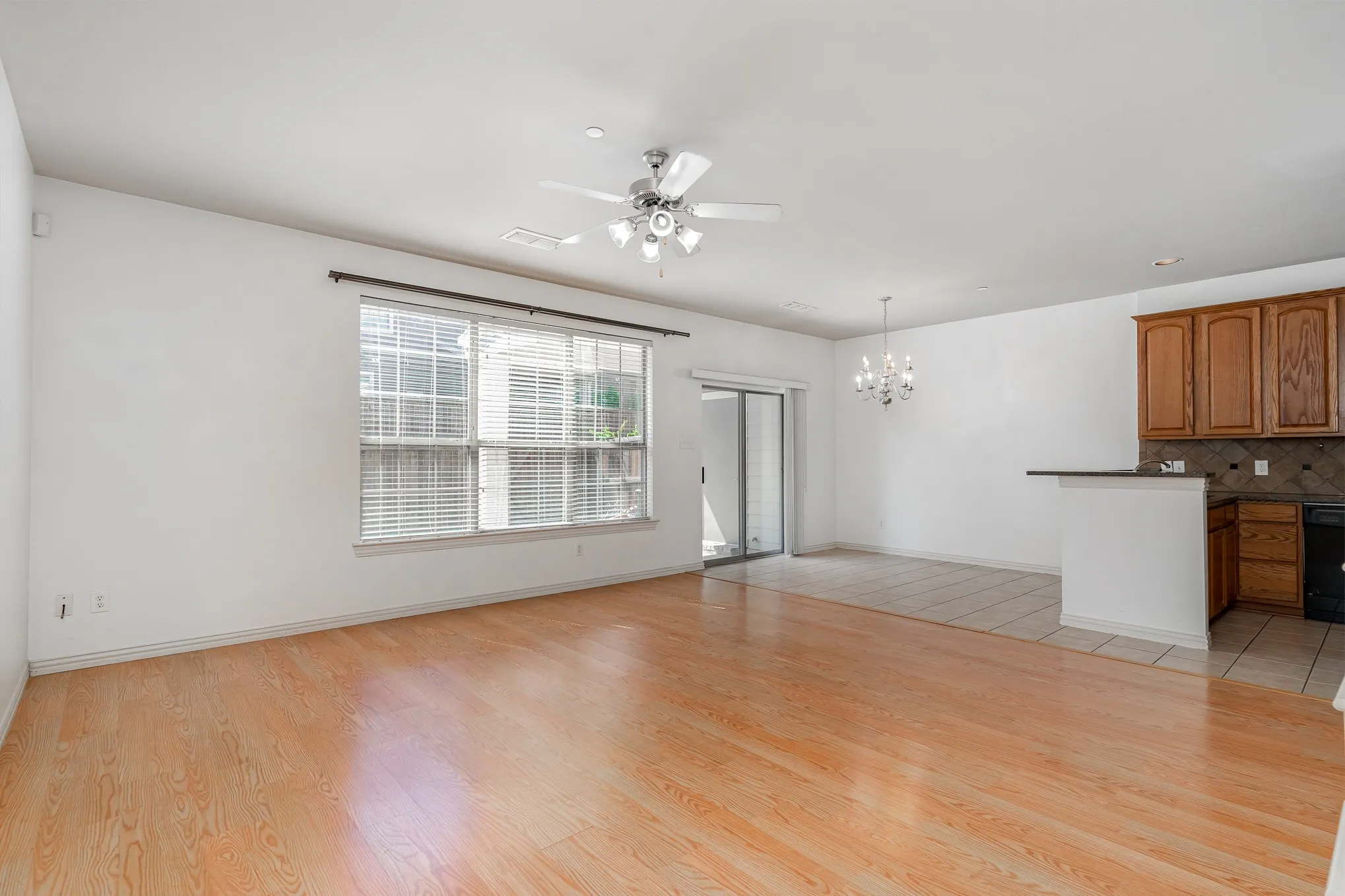Unfurnished living room featuring ceiling fan with notable chandelier and light hardwood / wood-style flooring
