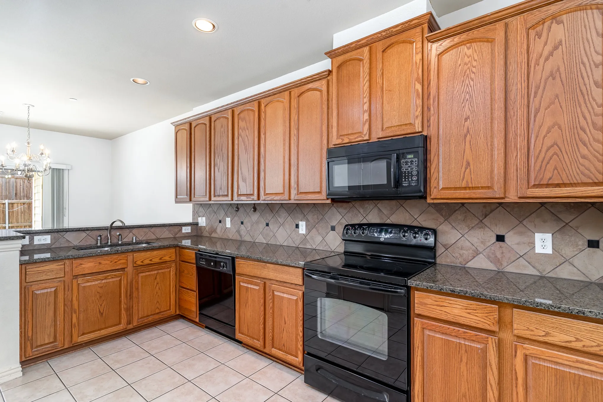 Kitchen with black appliances, backsplash, light tile floors, sink, and a chandelier