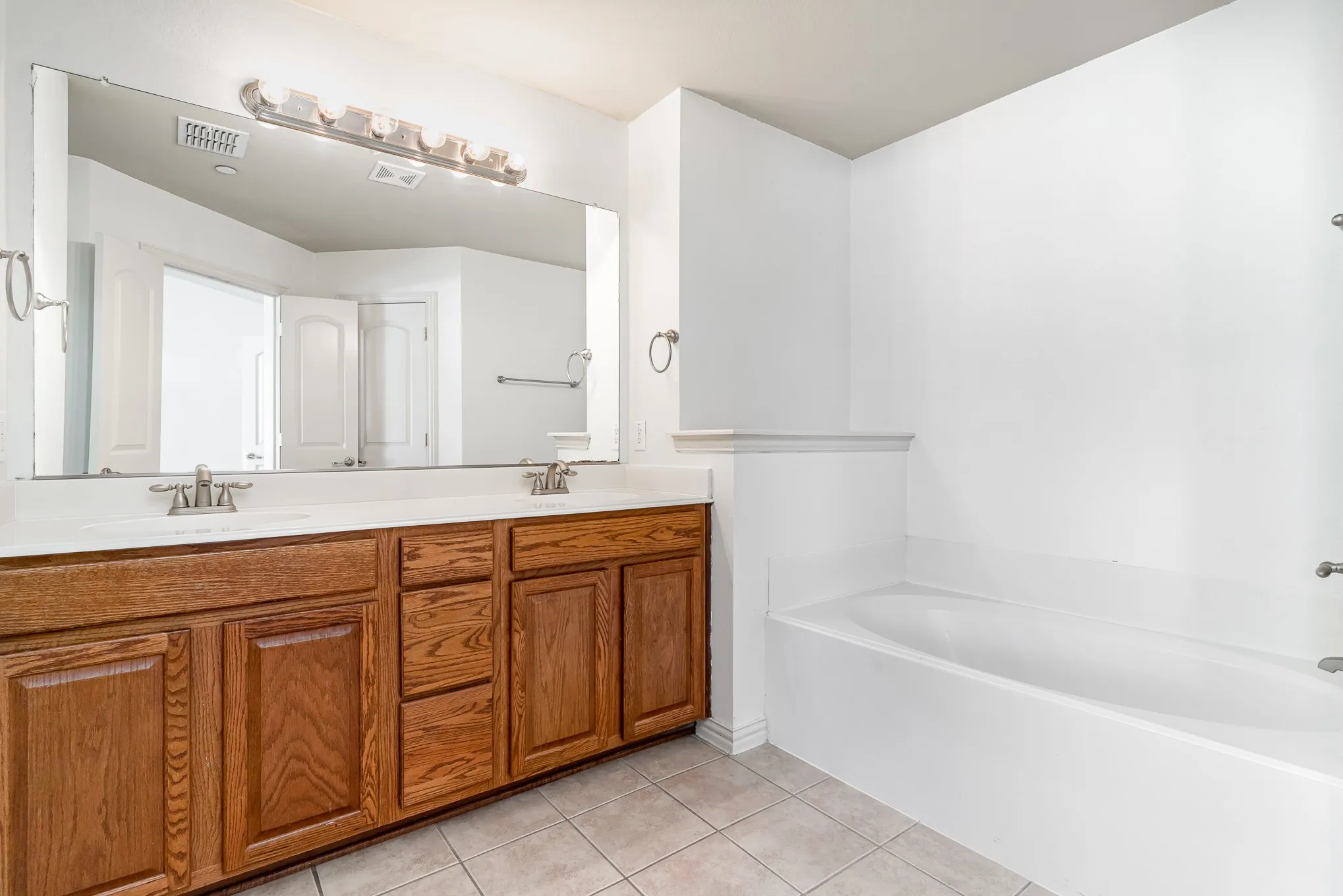 Bathroom featuring tile flooring, oversized vanity, dual sinks, and a bathtub