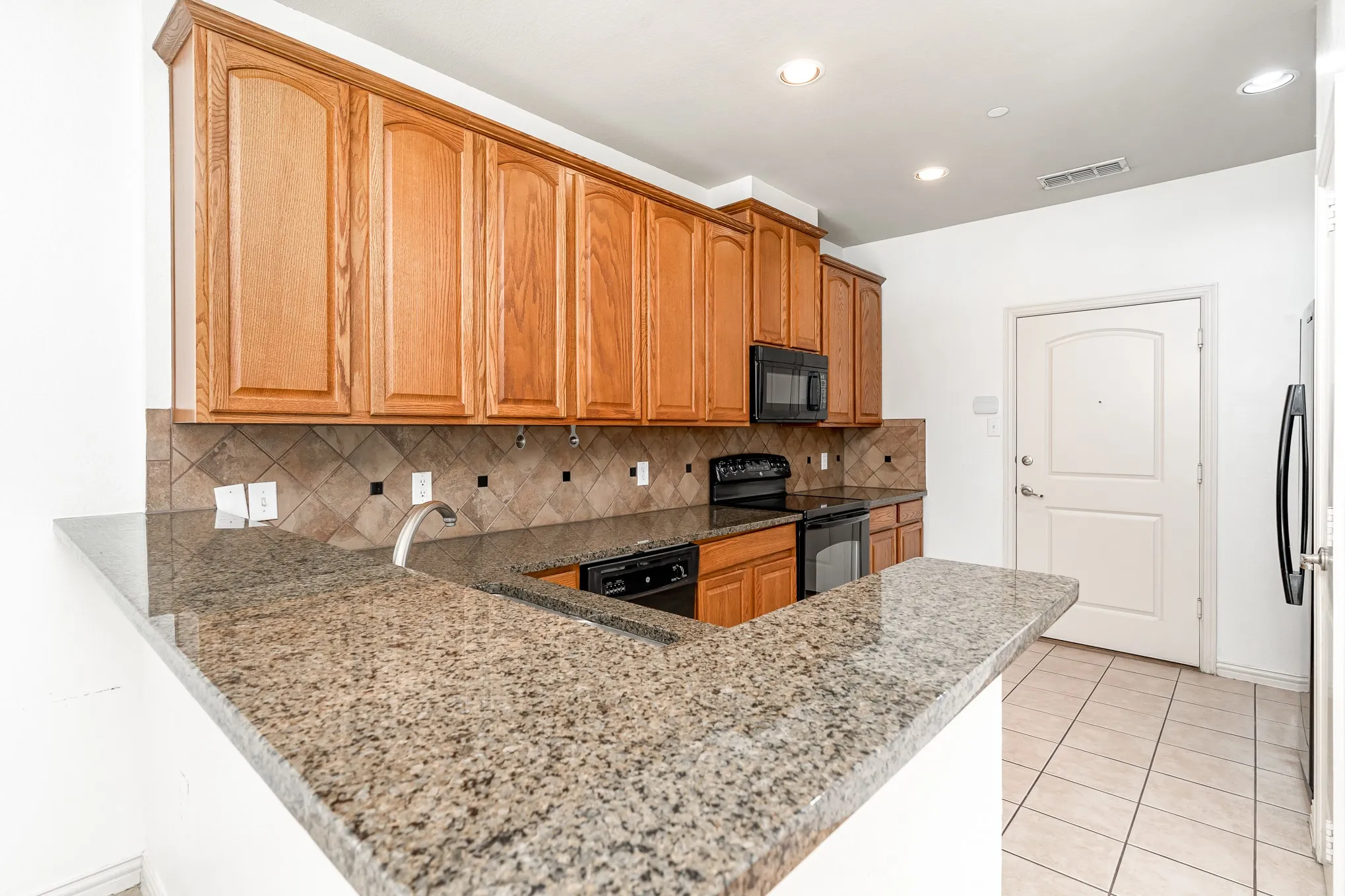 Kitchen with light stone counters, backsplash, black appliances, sink, and light tile floors