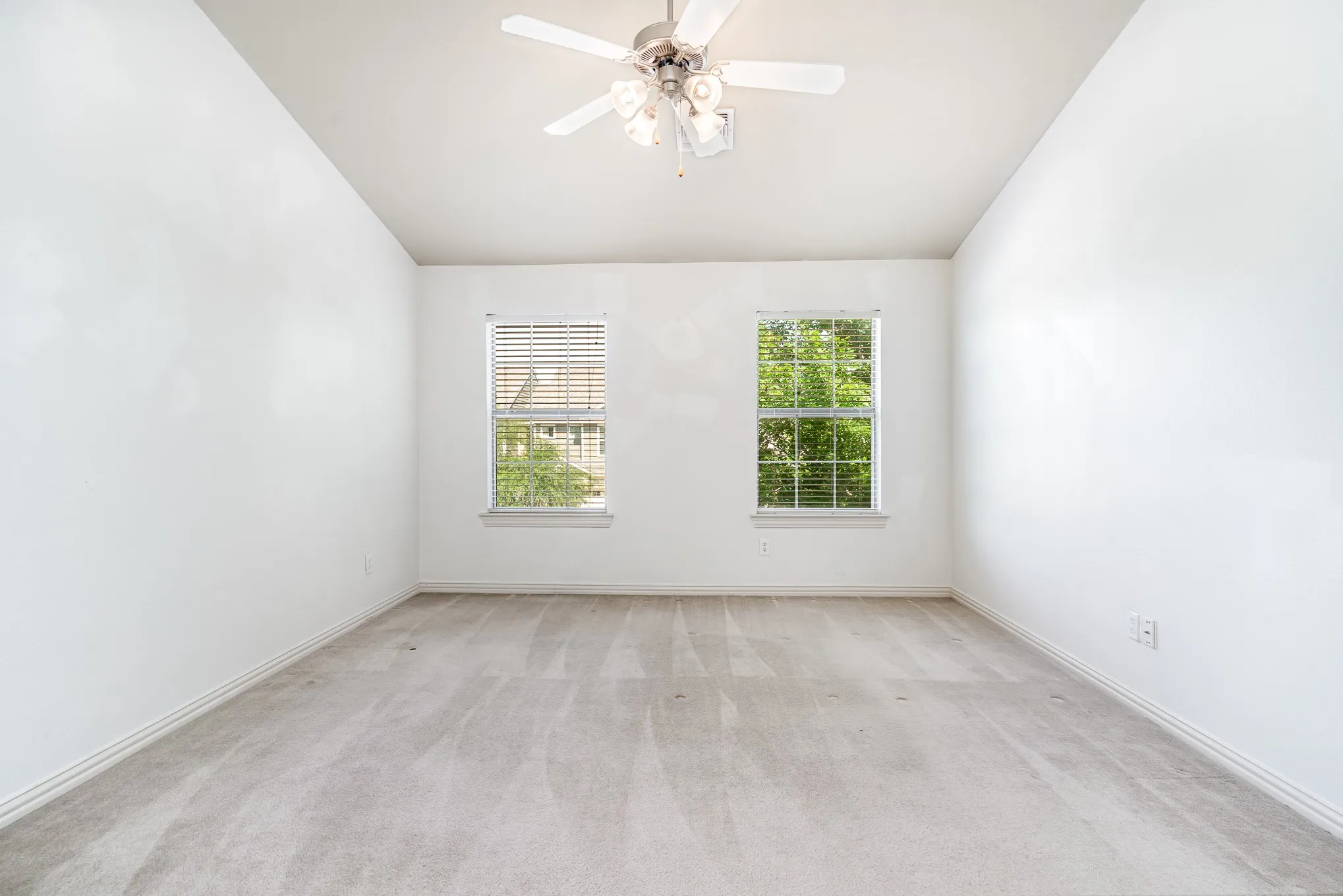 Carpeted empty room featuring ceiling fan and lofted ceiling