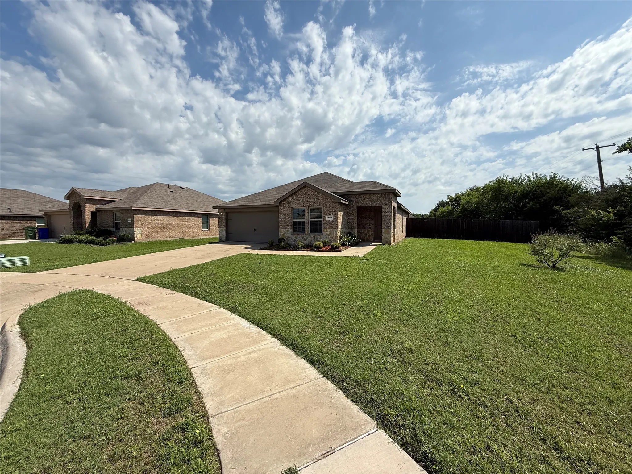 Single-story home featuring a brick facade with stone accents, an attached garage, a concrete driveway, and a concrete pathway