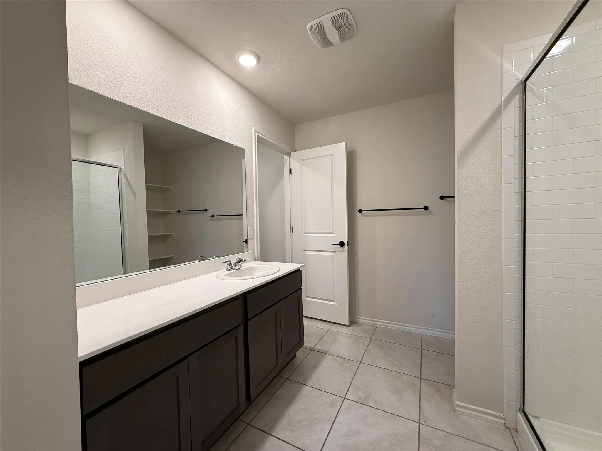 Bathroom featuring a single vanity with dark cabinetry, a white countertop, and a large wall-mounted mirror